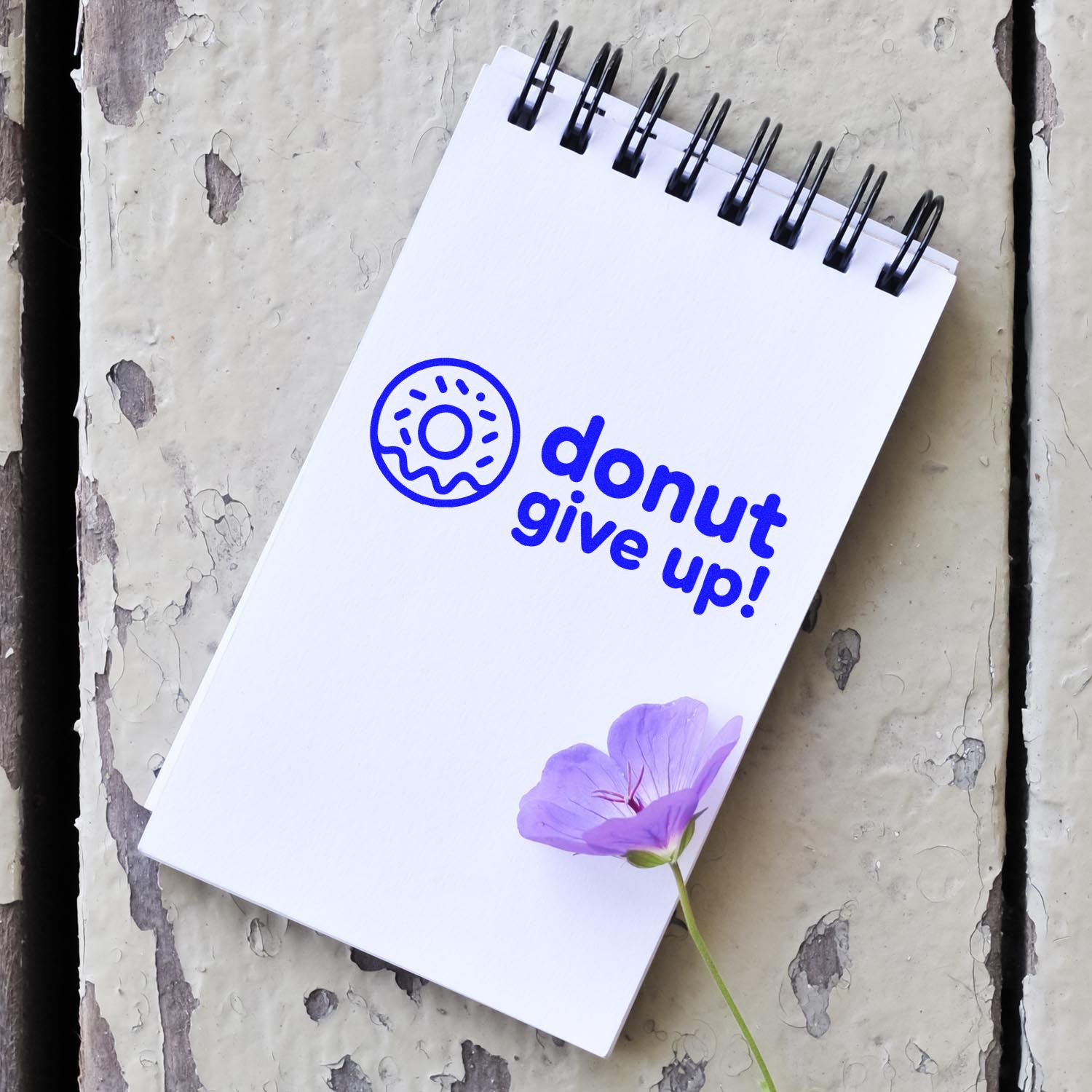 Custom rubber stamp design with donut give up message on a spiral notepad, featuring a donut icon and flower accent.
