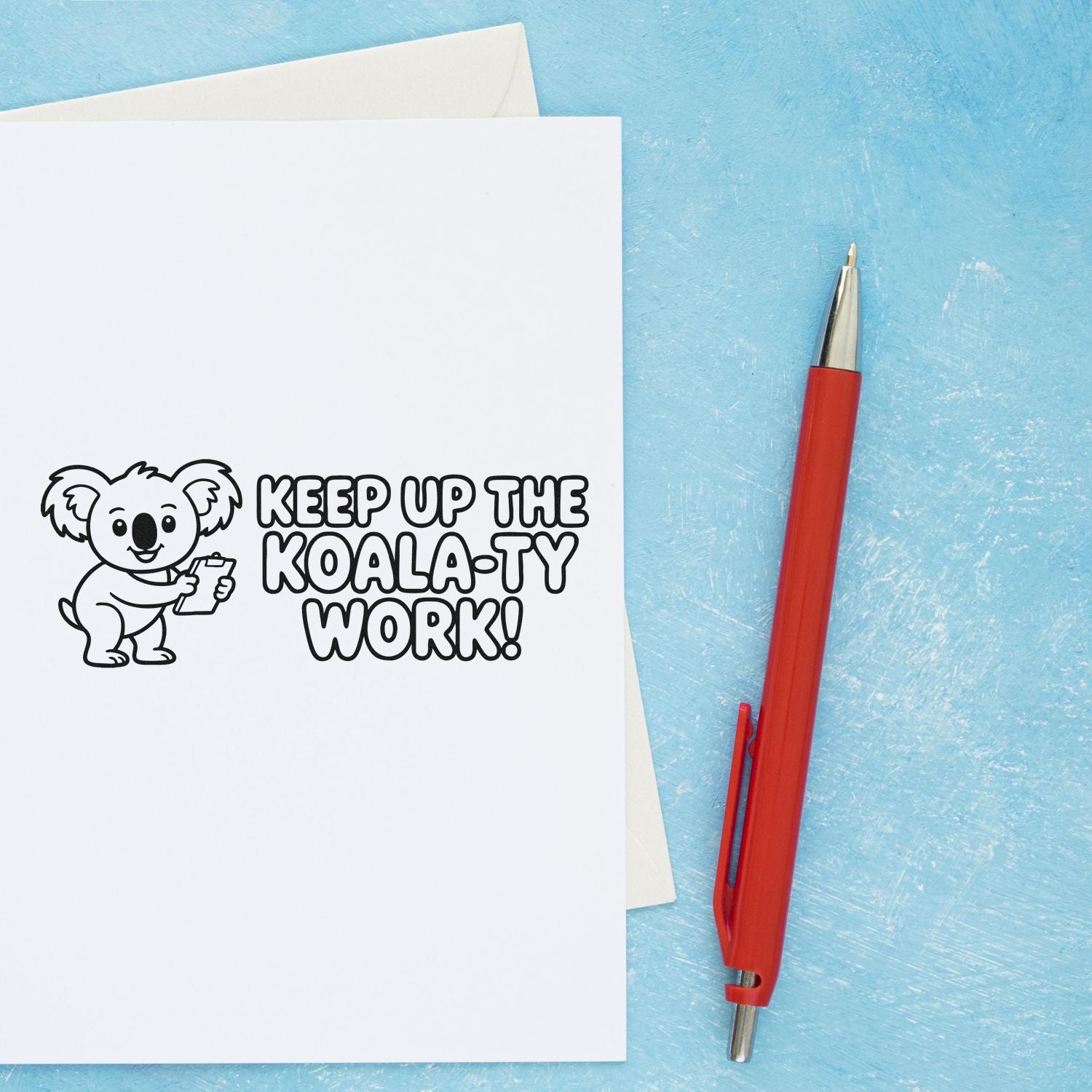 Koala rubber stamp impression with Keep Up the Koala-ty Work on a greeting card beside a red pen.