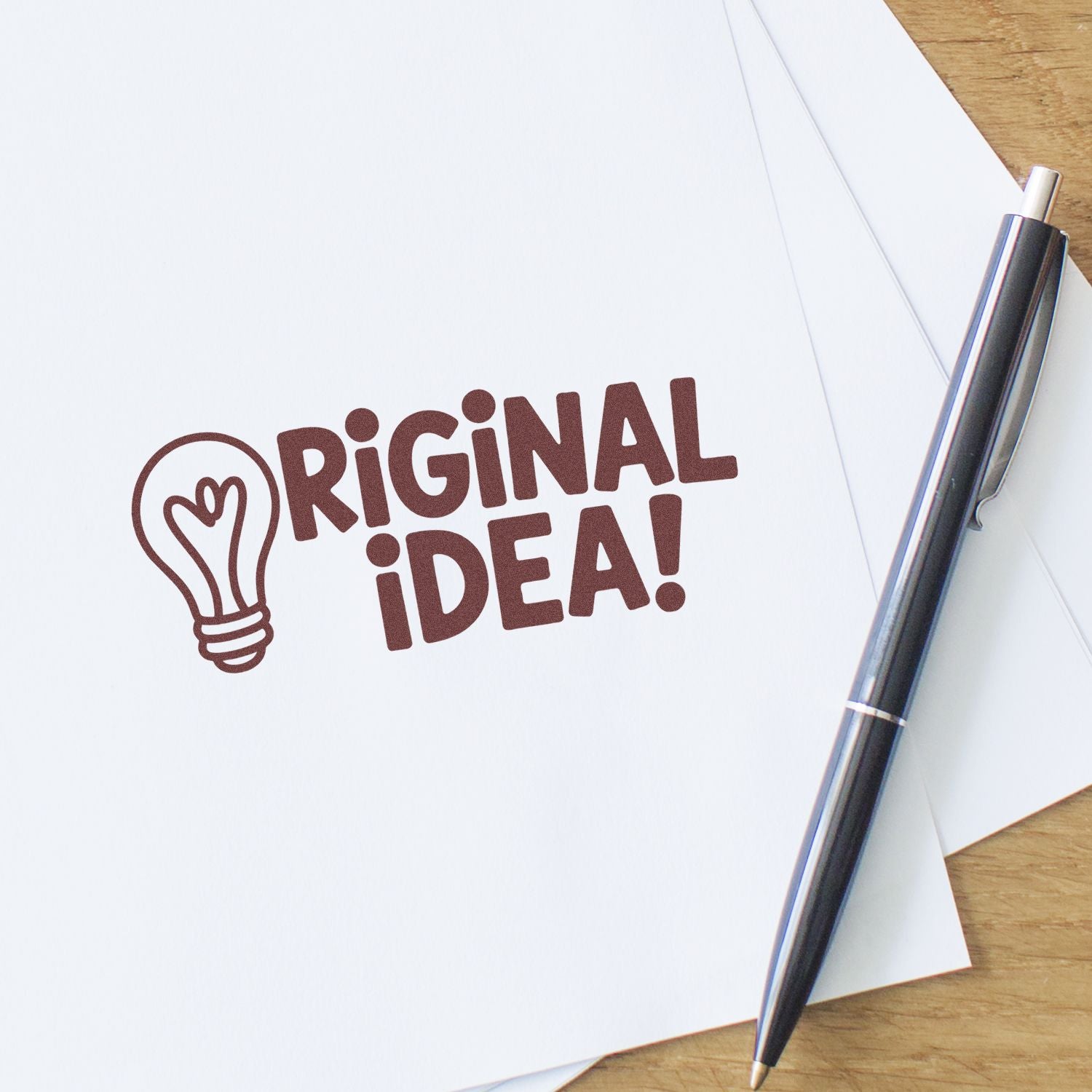 Custom rubber stamp design with "Original Idea!" lightbulb icon stamped on paper beside a pen