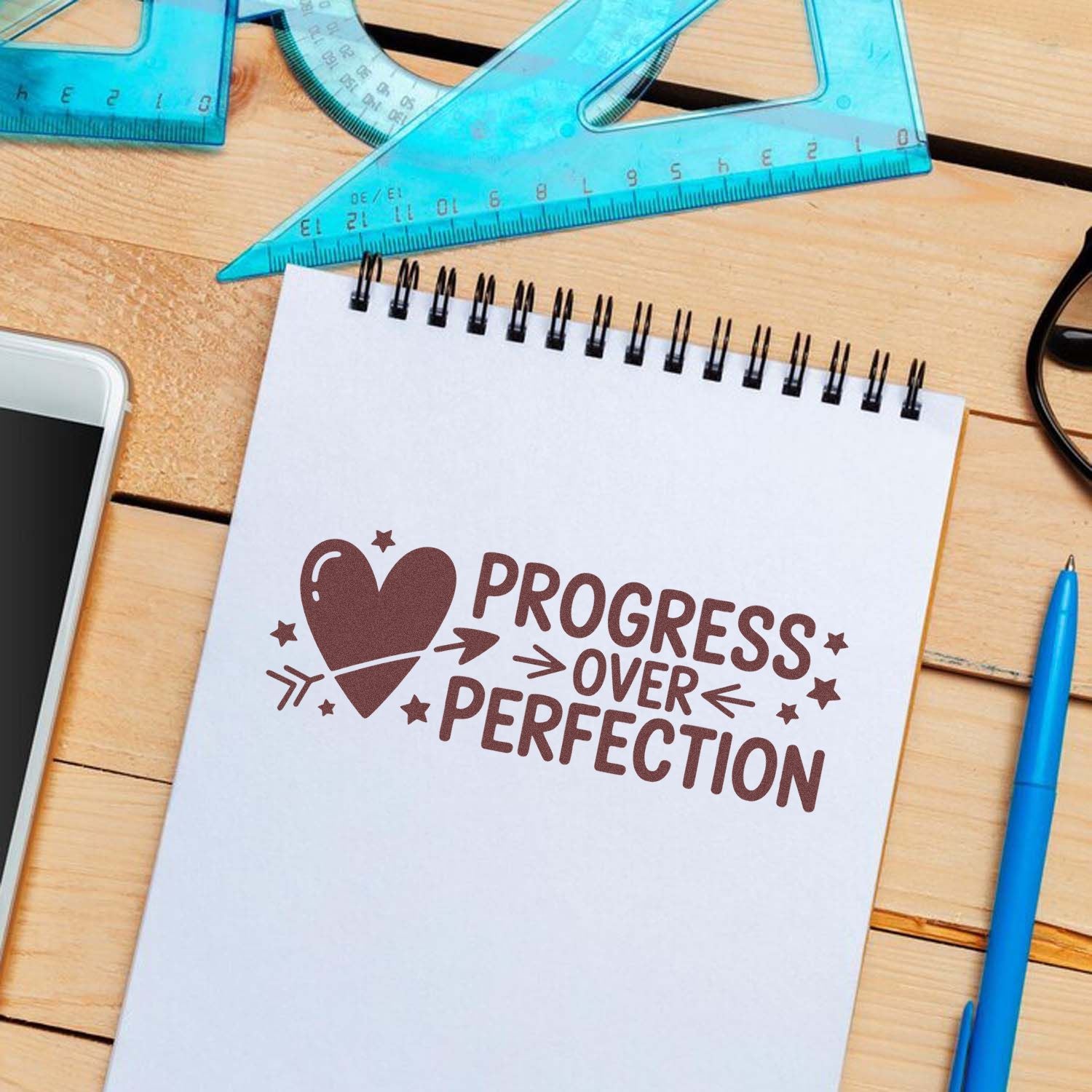 Progress over perfection rubber stamp design on notebook, ideal for motivational planner and craft projects.