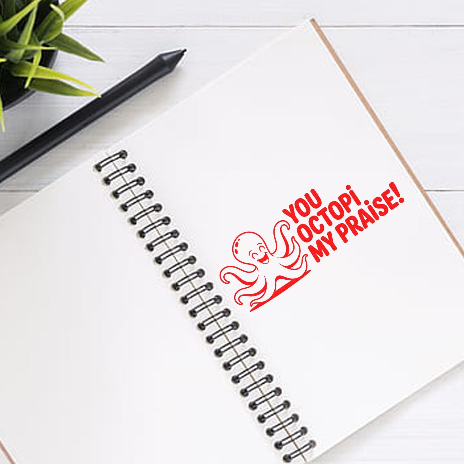 Red octopus rubber stamp reading You octopi my praise! on a notebook, showcasing a playful custom stamp design.