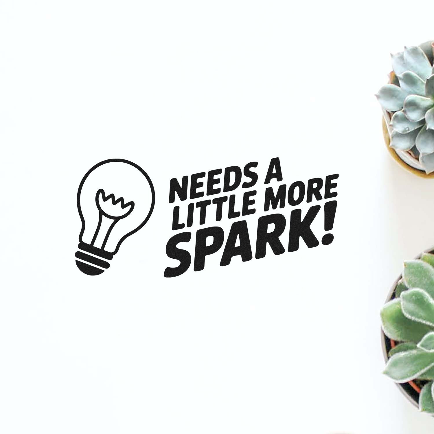 Rubber stamp design with light bulb icon and the phrase Needs a little more spark! for crafting, journaling, or packaging.