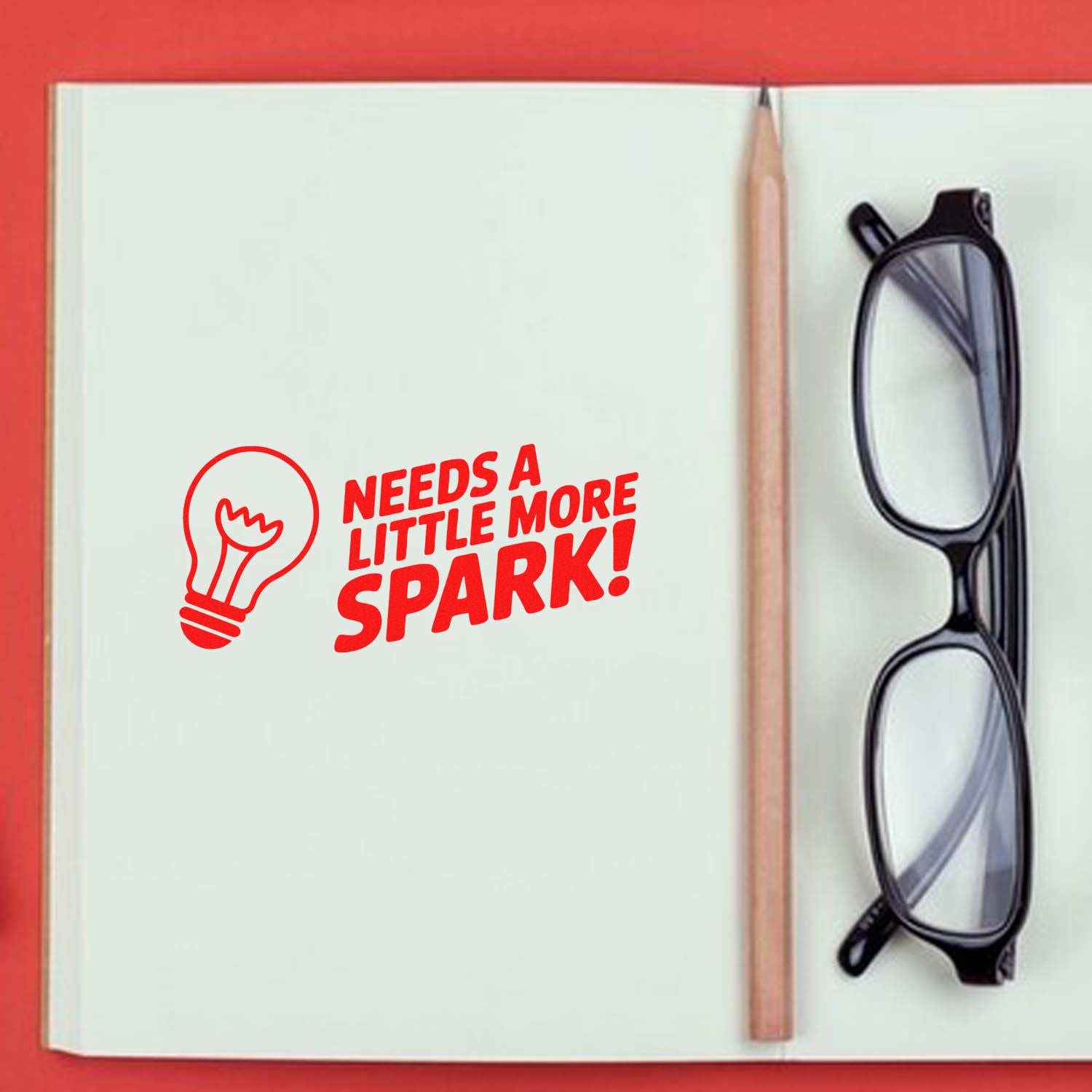 Custom rubber stamp design reading Needs a Little More Spark! with lightbulb icon in an open notebook.