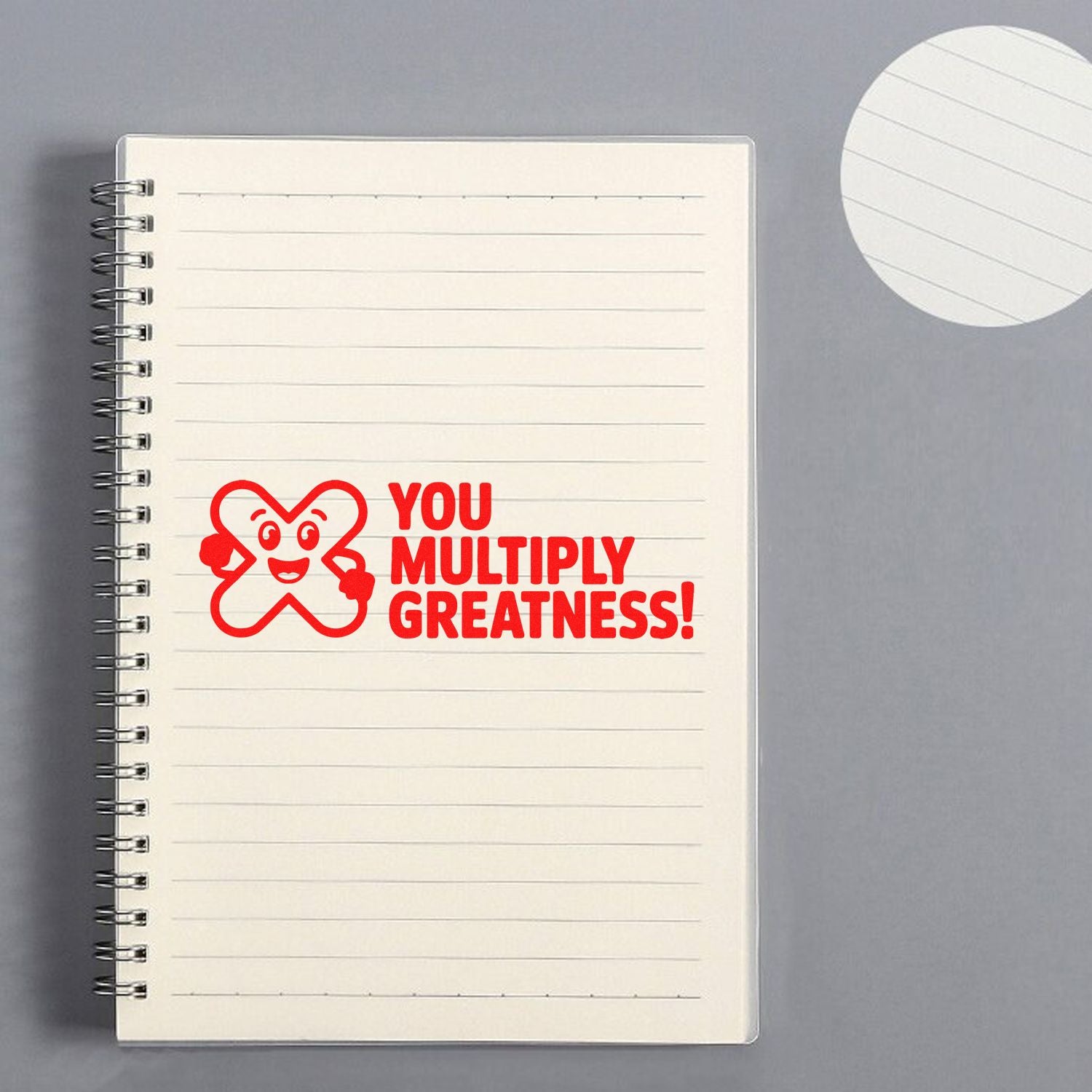 Custom motivational rubber stamp saying You Multiply Greatness! stamped in red on a lined notebook page.