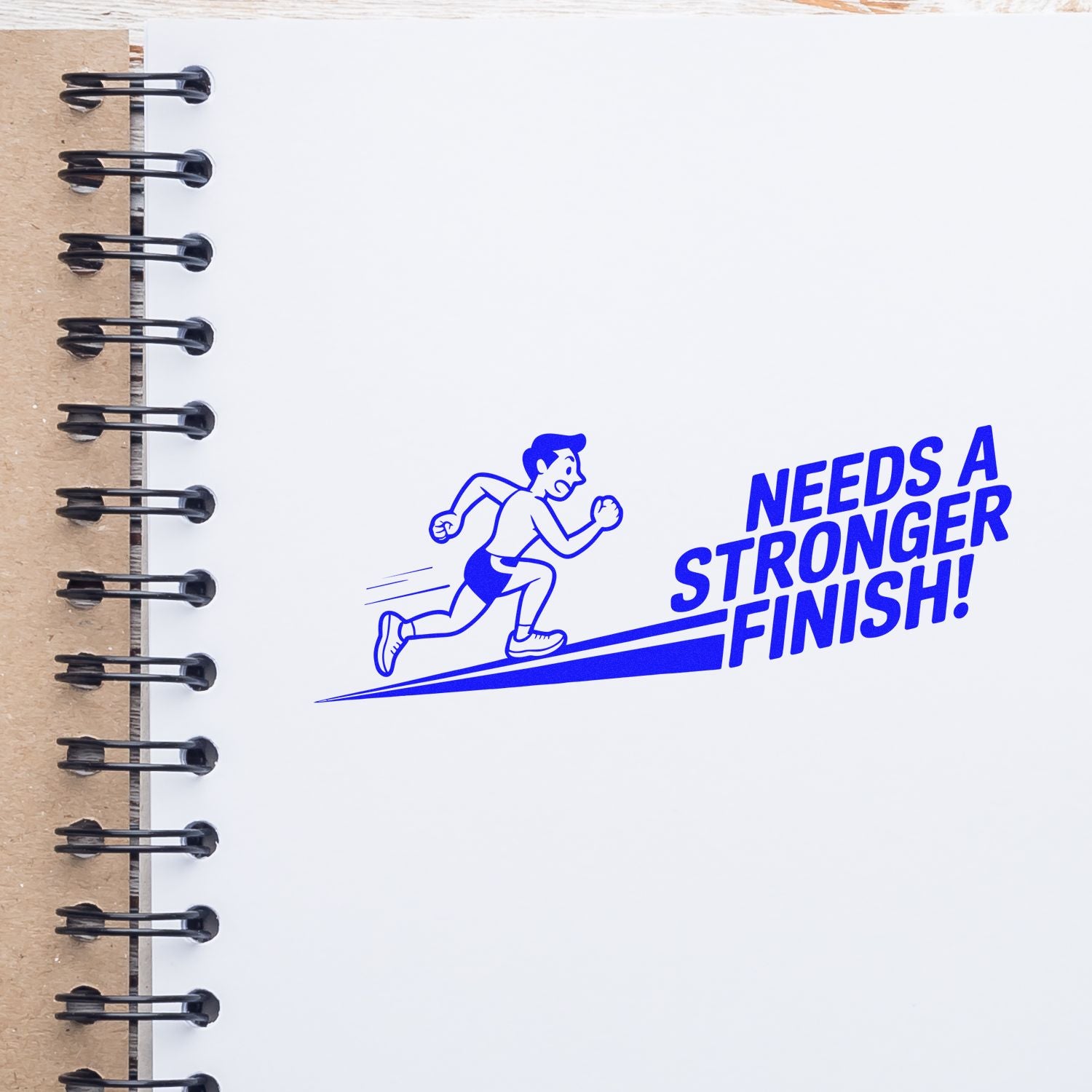 Custom rubber stamp impression reading Needs a Stronger Finish! with runner graphic in a spiral notebook.