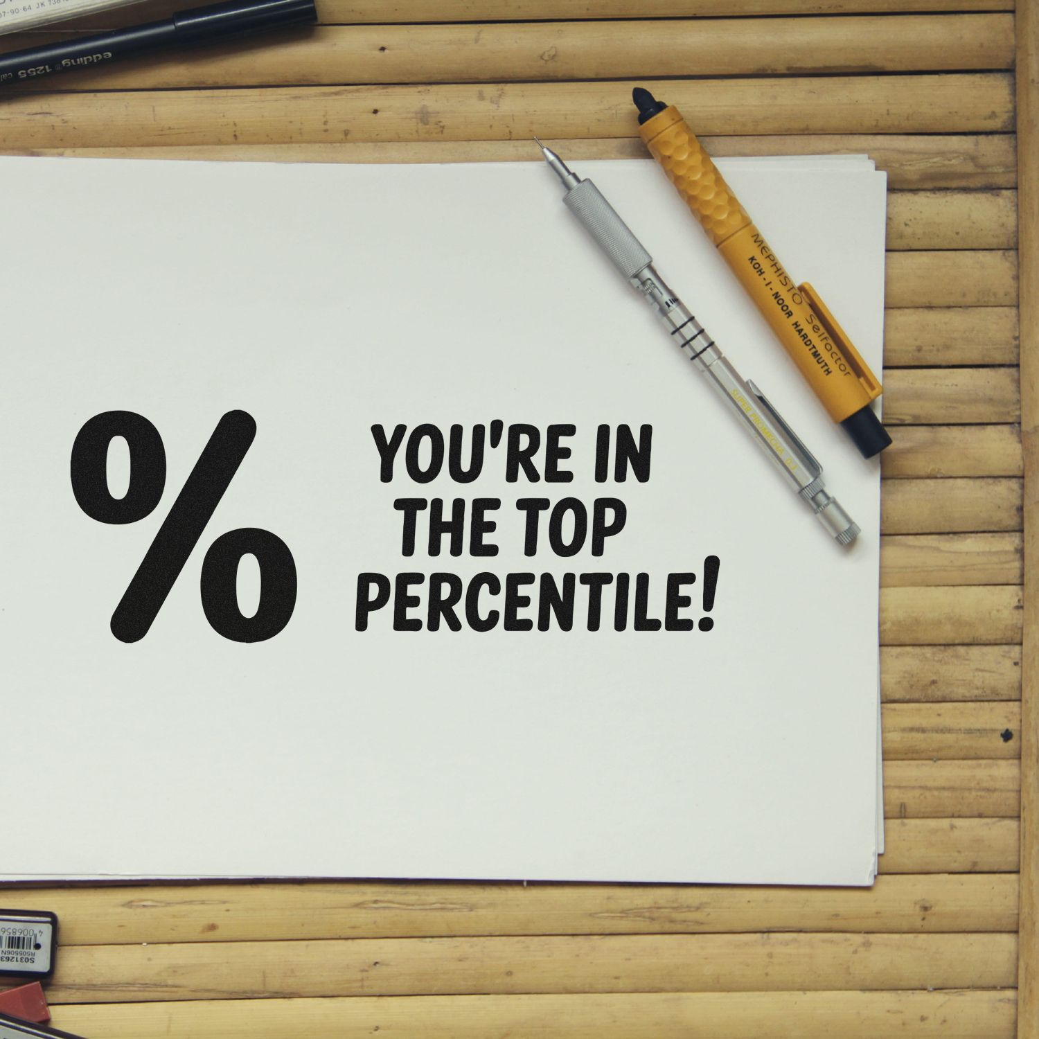 Custom rubber stamp design reading Youre in the top percentile! on paper with drafting tools.