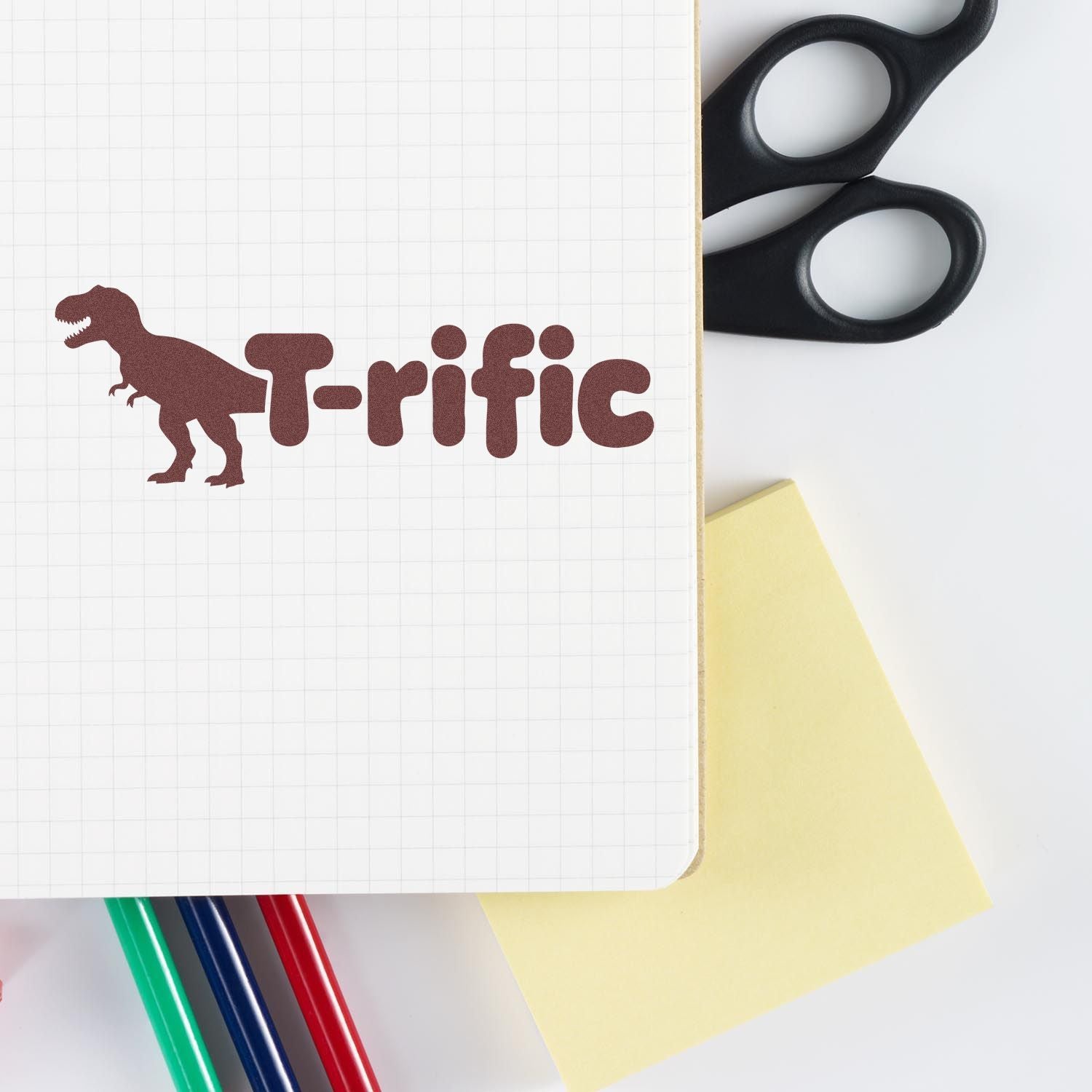T-rific T-Rex rubber stamp design on notebook with office supplies, perfect for teacher craft projects.