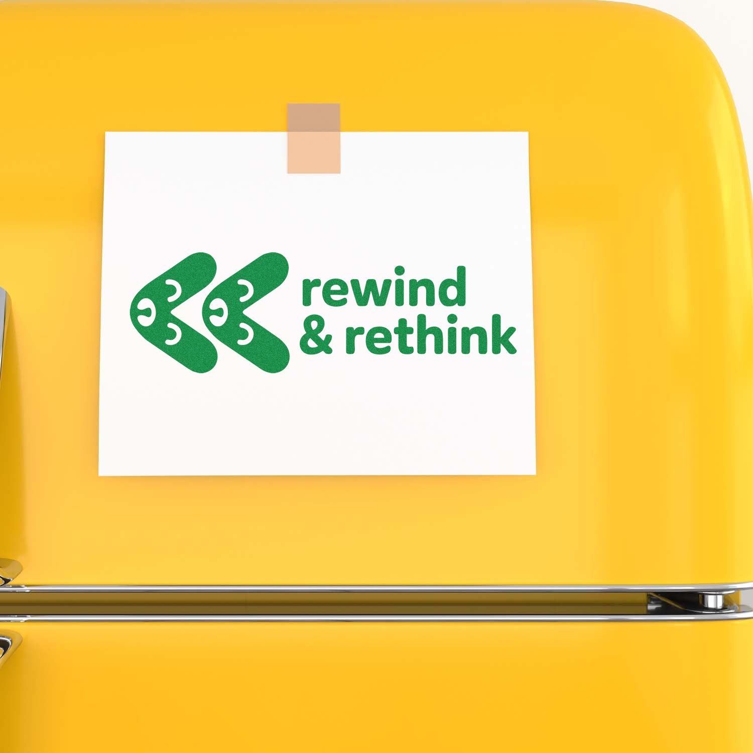 Green rewind & rethink rubber stamp design on white paper taped to a bright yellow surface.