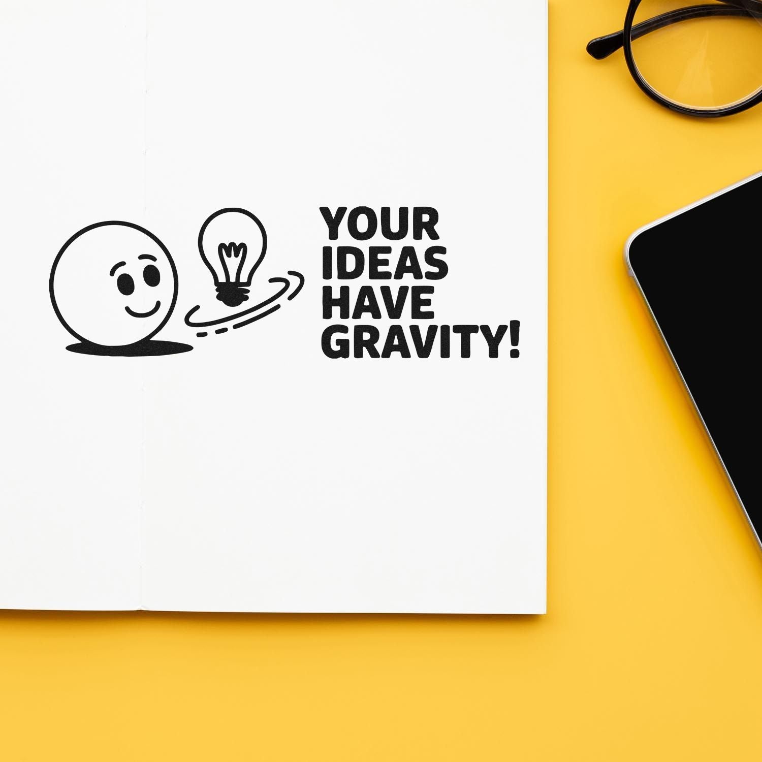 Motivational rubber stamp design with Your ideas have gravity! and lightbulb graphic on a notebook page.