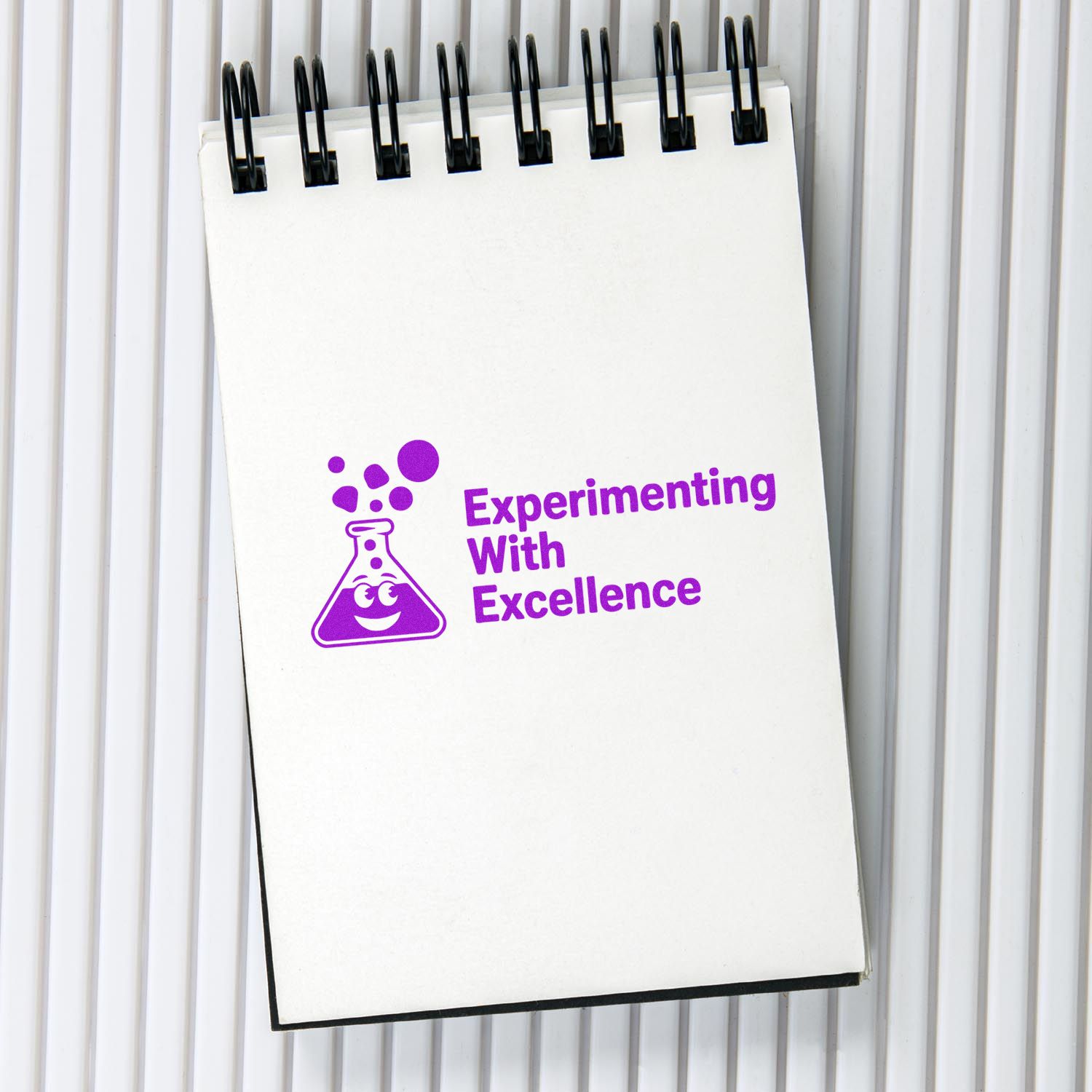 Custom rubber stamp design on notebook reading Experimenting With Excellence with smiling lab flask icon.