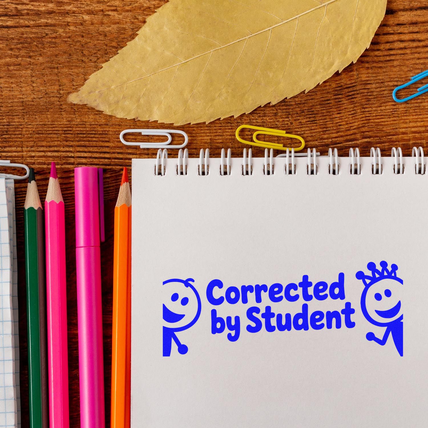 Student correction rubber stamp reading Corrected by Student on notebook with pencils and school supplies.