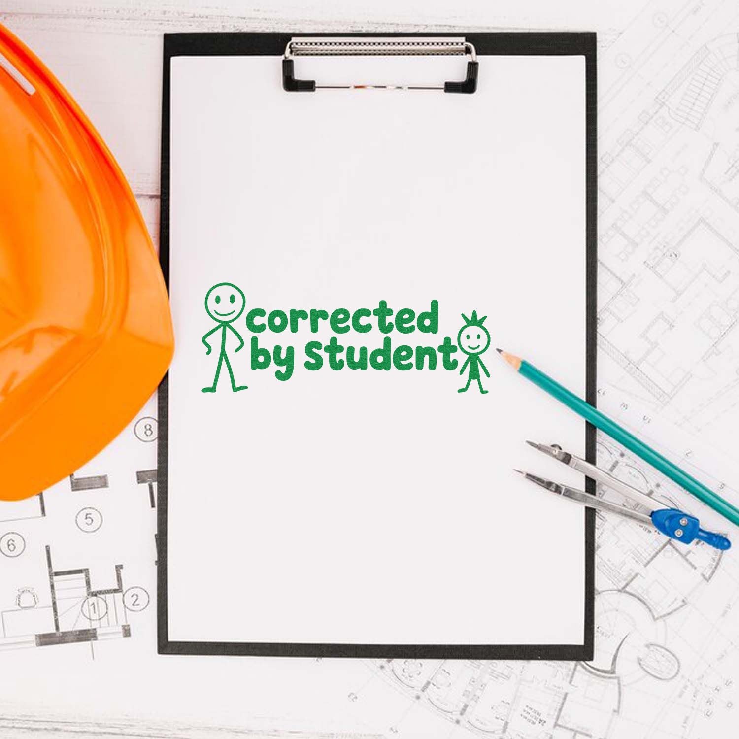 Corrected by Student rubber stamp on clipboard for teacher grading, with hard hat, pencils and blueprint plans.