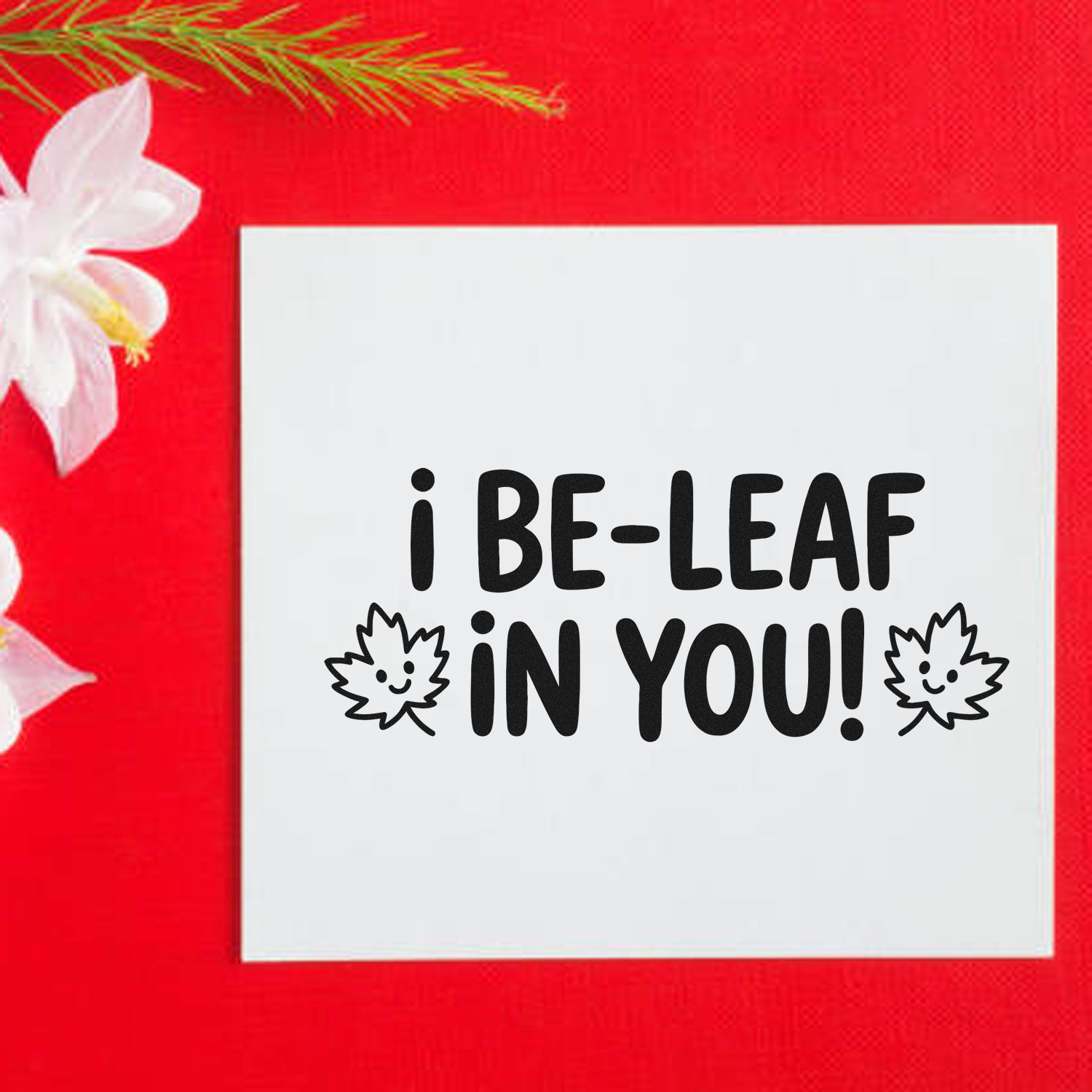 Encouraging rubber stamp design reading I be-leaf in you! with smiling leaf icons on a white card.