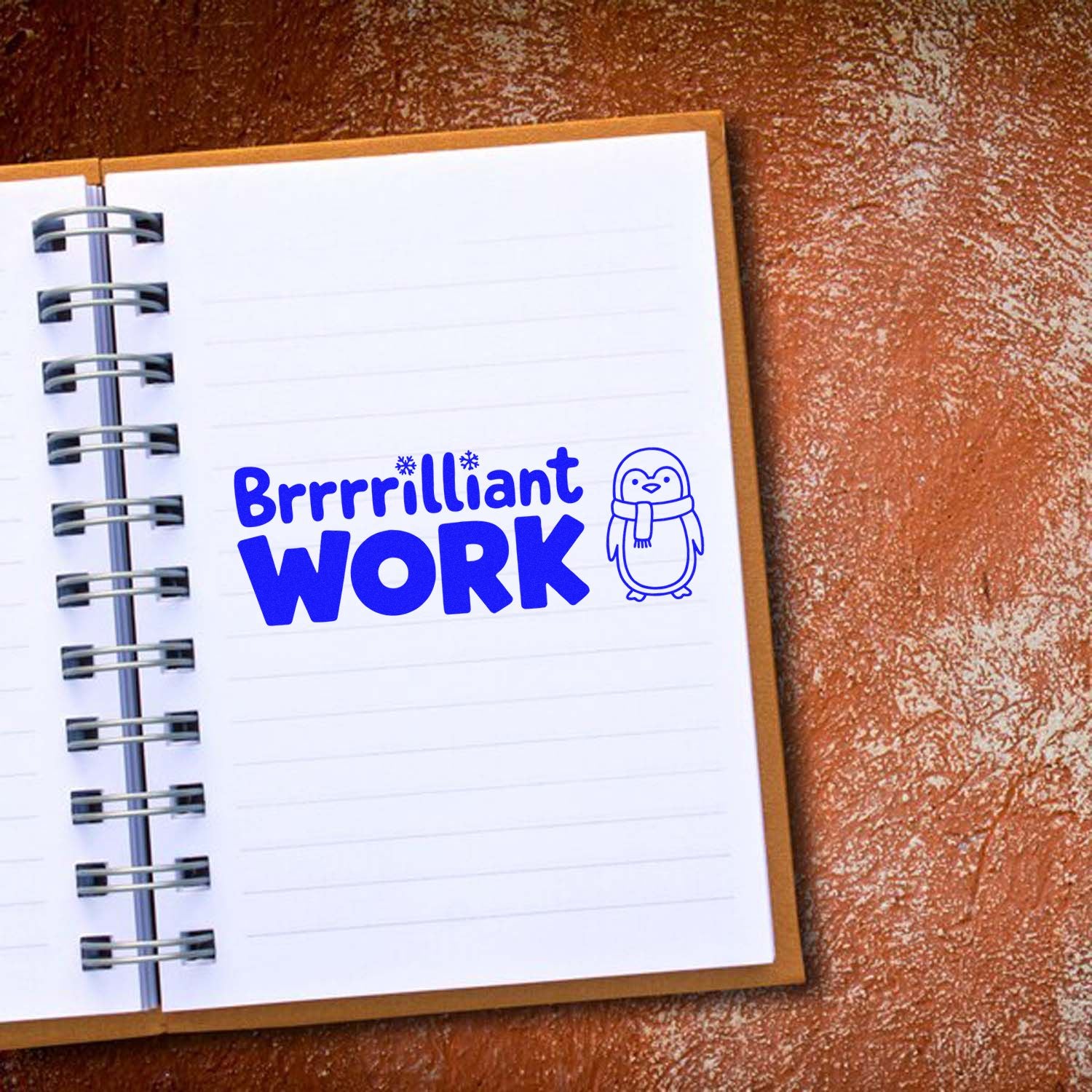 Brrrilliant Work penguin rubber stamp on notebook, ideal for winter-themed teacher rewards and office praise.