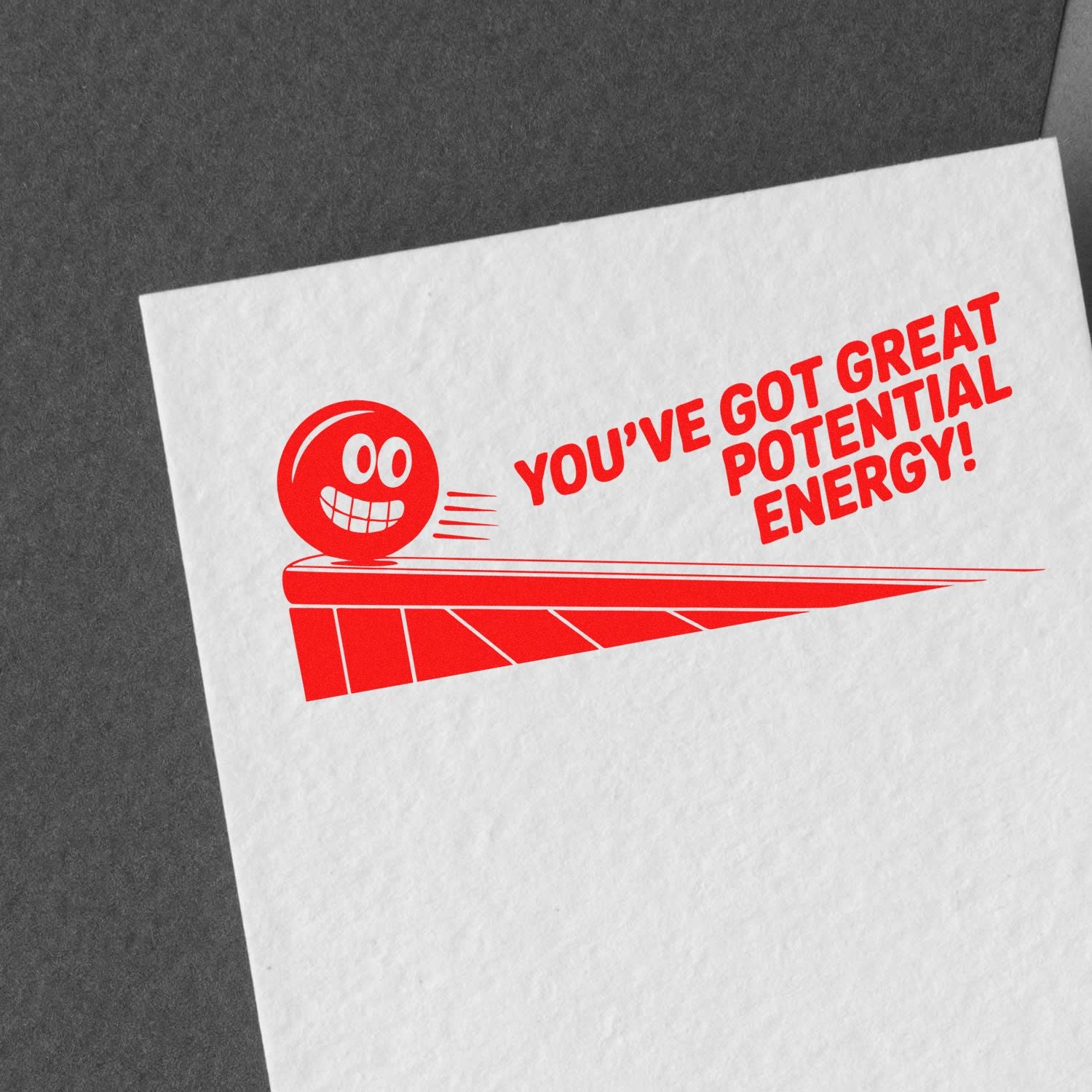 Red motivational rubber stamp reading Youve got great potential energy! on white paper with a smiling icon.