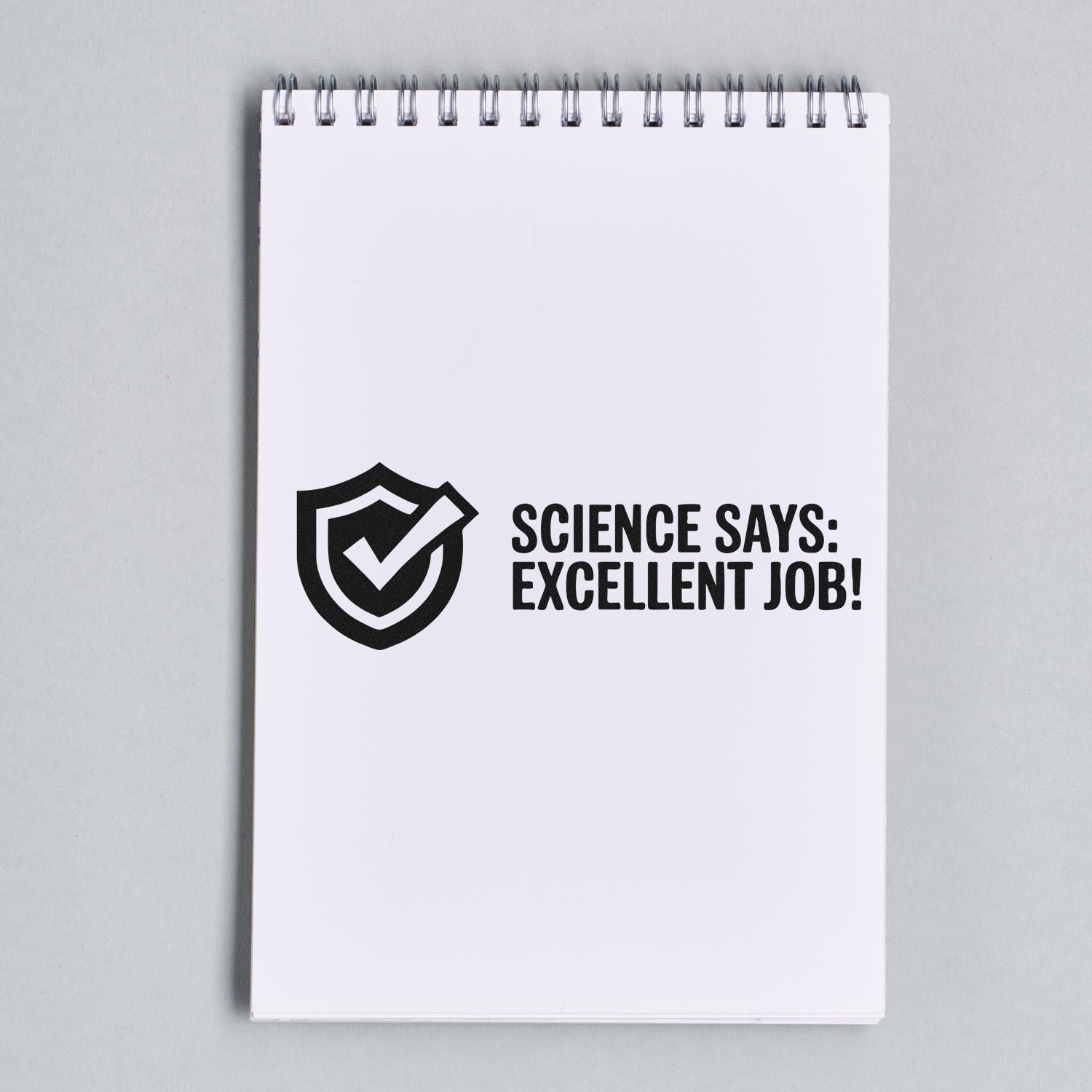 Science says excellent job rubber stamp with shield checkmark on a spiral notebook page.