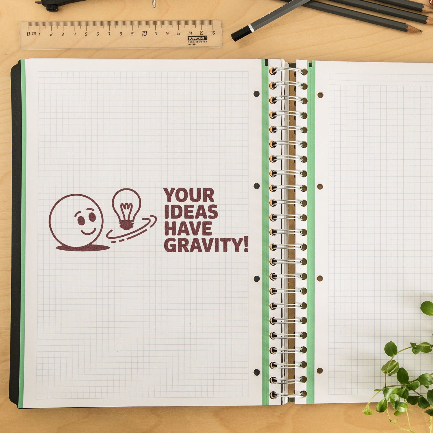 Custom rubber stamp design reading Your ideas have gravity! on an open notebook with smiley face and lightbulb.