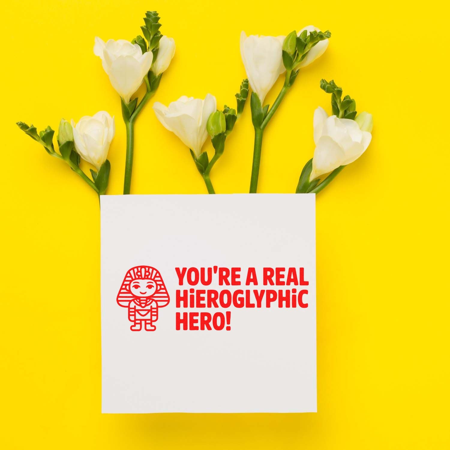 Rubber stamp design reading Youre a real hieroglyphic hero! with white flowers on a bright yellow background.