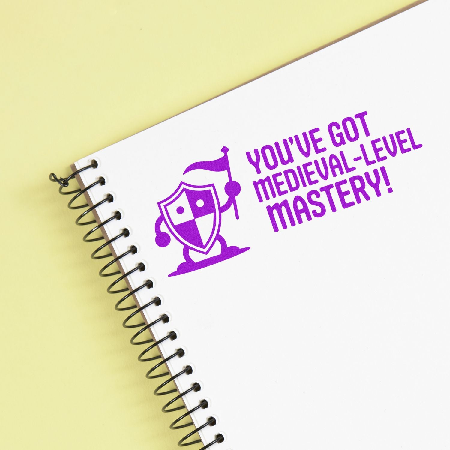 Custom medieval-themed rubber stamp with knight shield icon and Youve got medieval-level mastery! on notebook.
