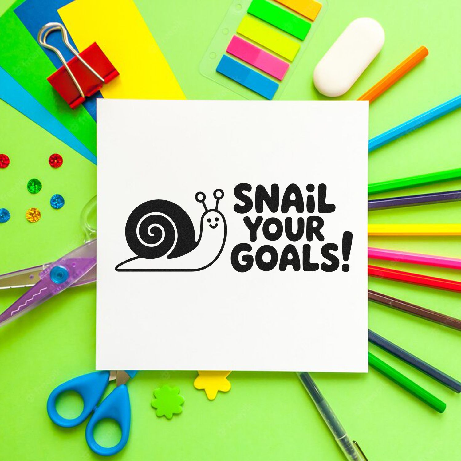 Cute snail rubber stamp design reading Snail Your Goals! on white paper, styled with colorful school and craft supplies.