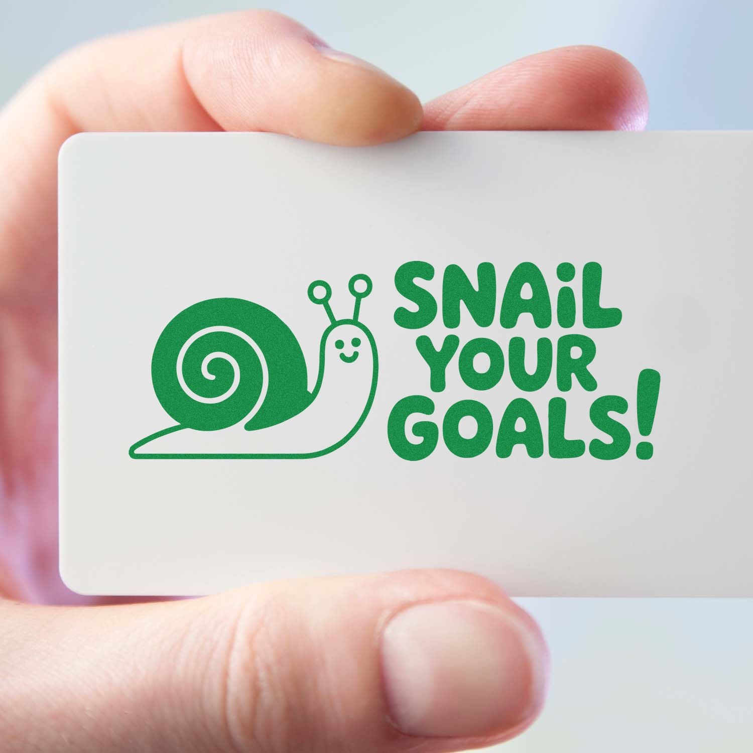 Hand holding custom rubber stamp design with snail graphic and Snail Your Goals! motivational phrase in green.