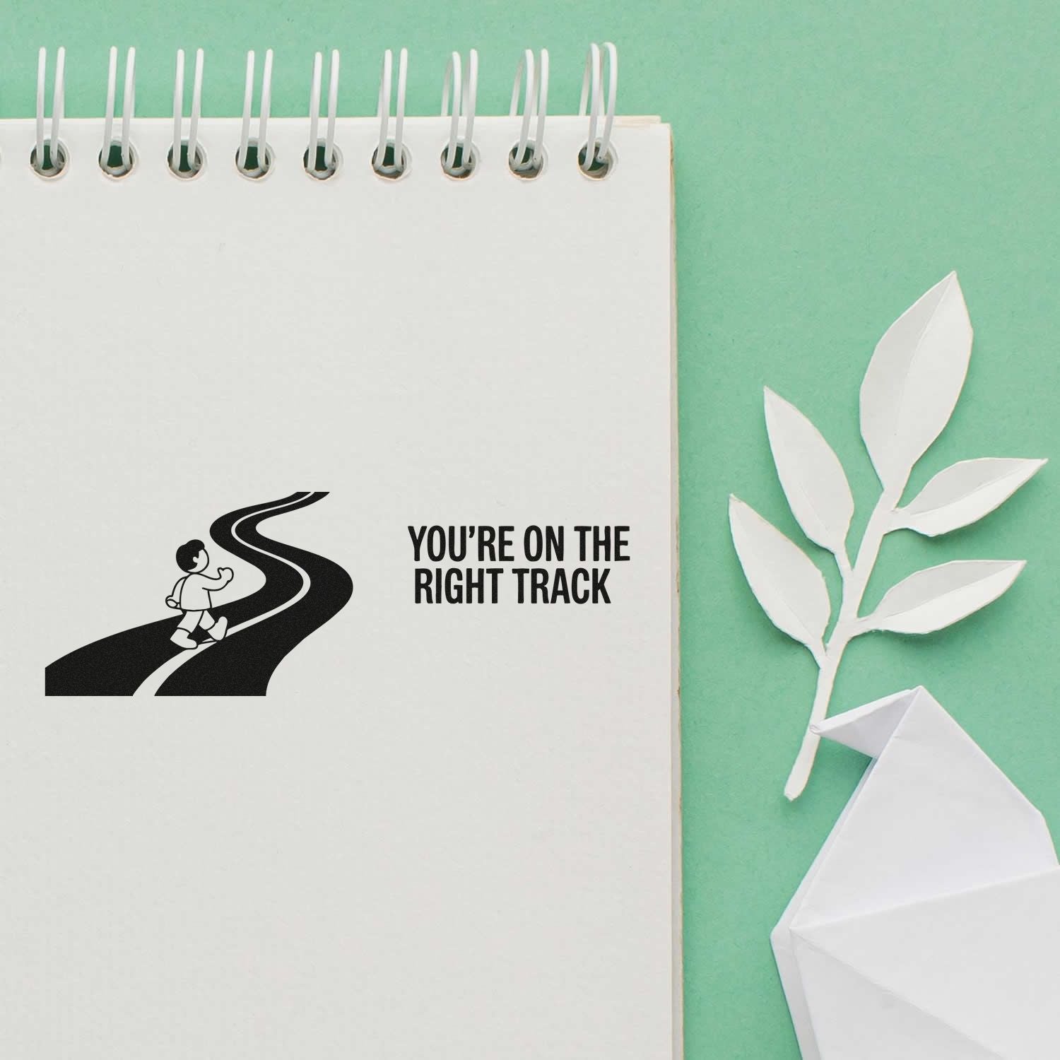 Motivational rubber stamp design saying Youre on the Right Track with road-and-walker icon on a notebook page.