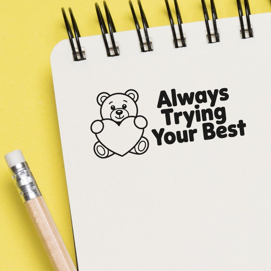 Motivational rubber stamp design with bear holding a heart and the phrase Always Trying Your Best on a notebook page.