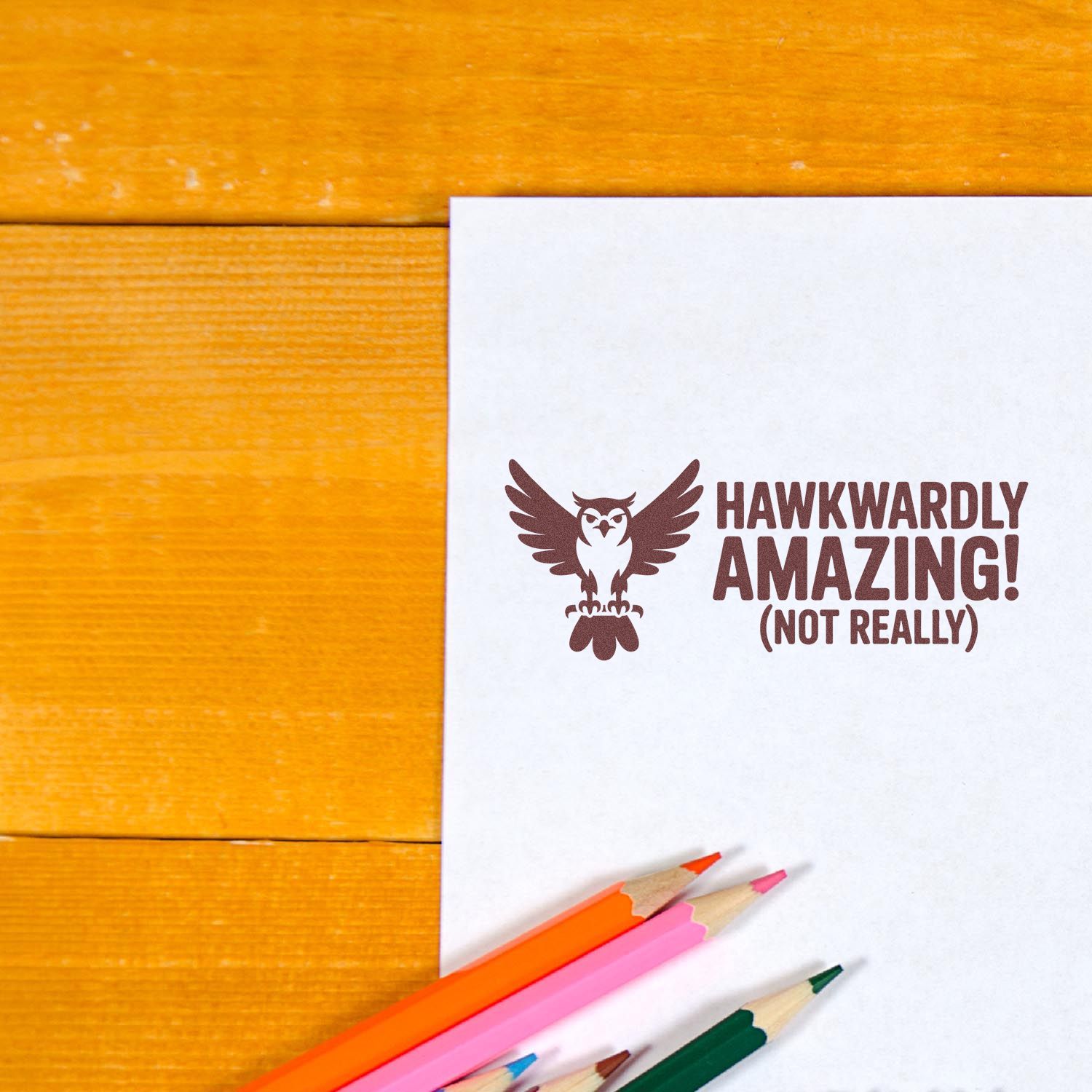 Funny owl rubber stamp on paper reading Hawkwardly Amazing! (Not Really) with colored pencils, ideal for playful stationery and cards.