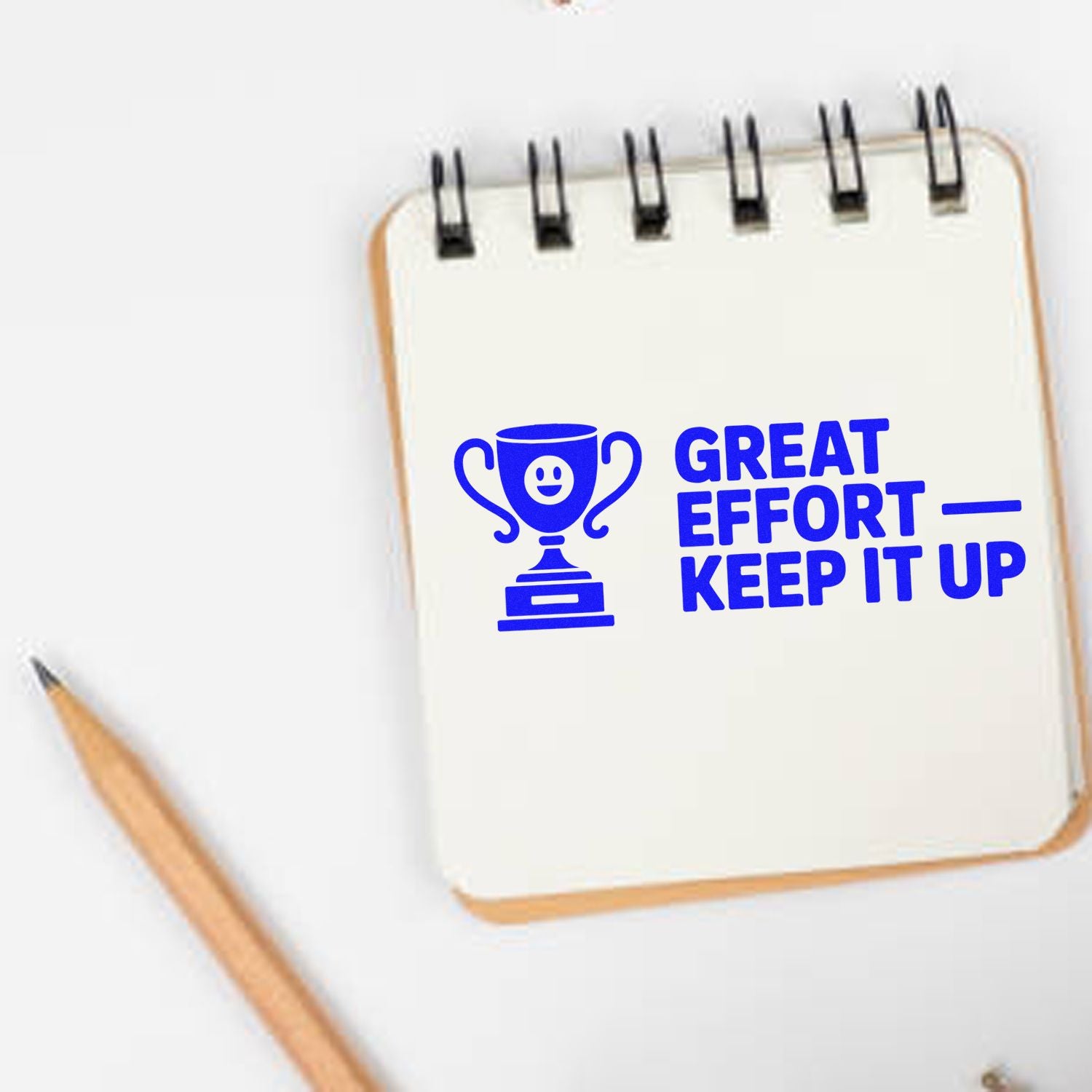 Blue rubber stamp reading Great Effort Keep It Up with trophy icon on notebook for motivational teacher feedback.