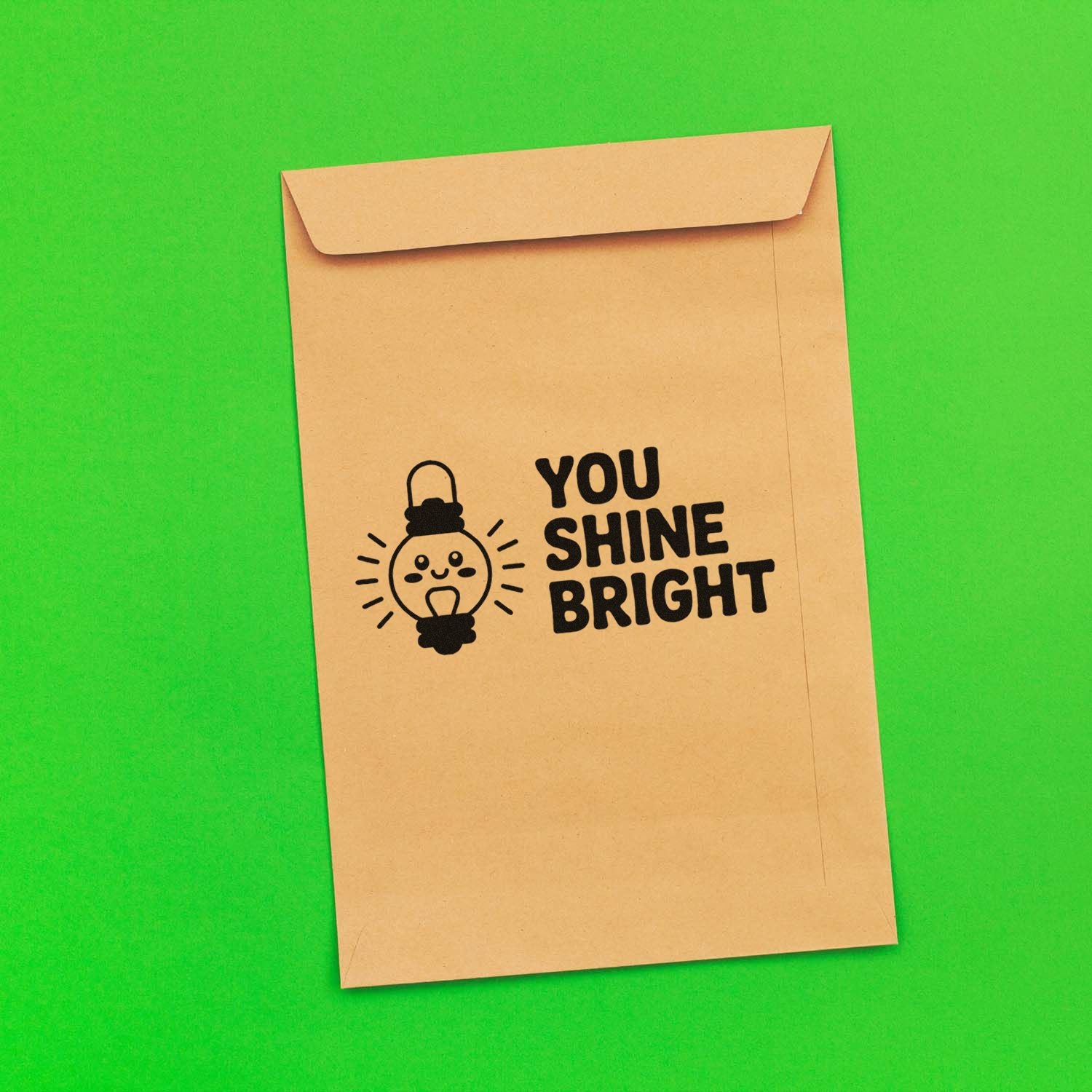 Rubber stamp design on kraft envelope with smiling light bulb and You Shine Bright message.