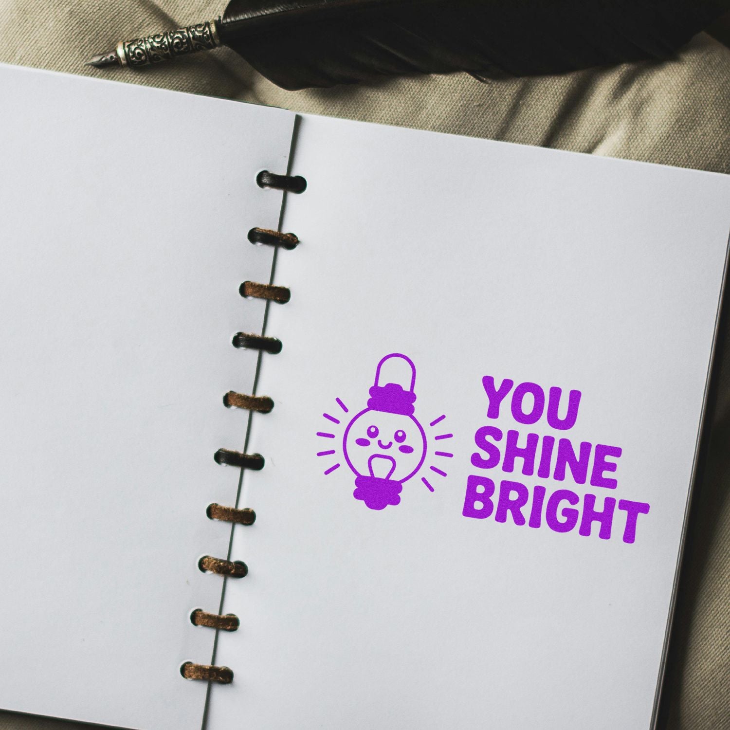 Custom rubber stamp design with You Shine Bright lightbulb graphic on a spiral notebook page.