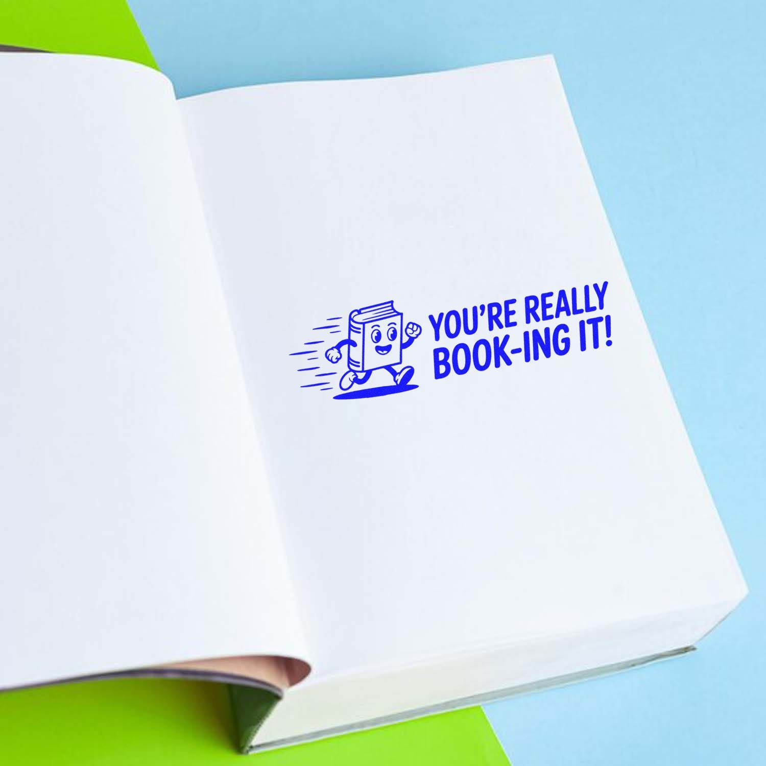 Custom rubber stamp on an open book reading Youre really book-ing it! for library, reading, and bookstore promotions.