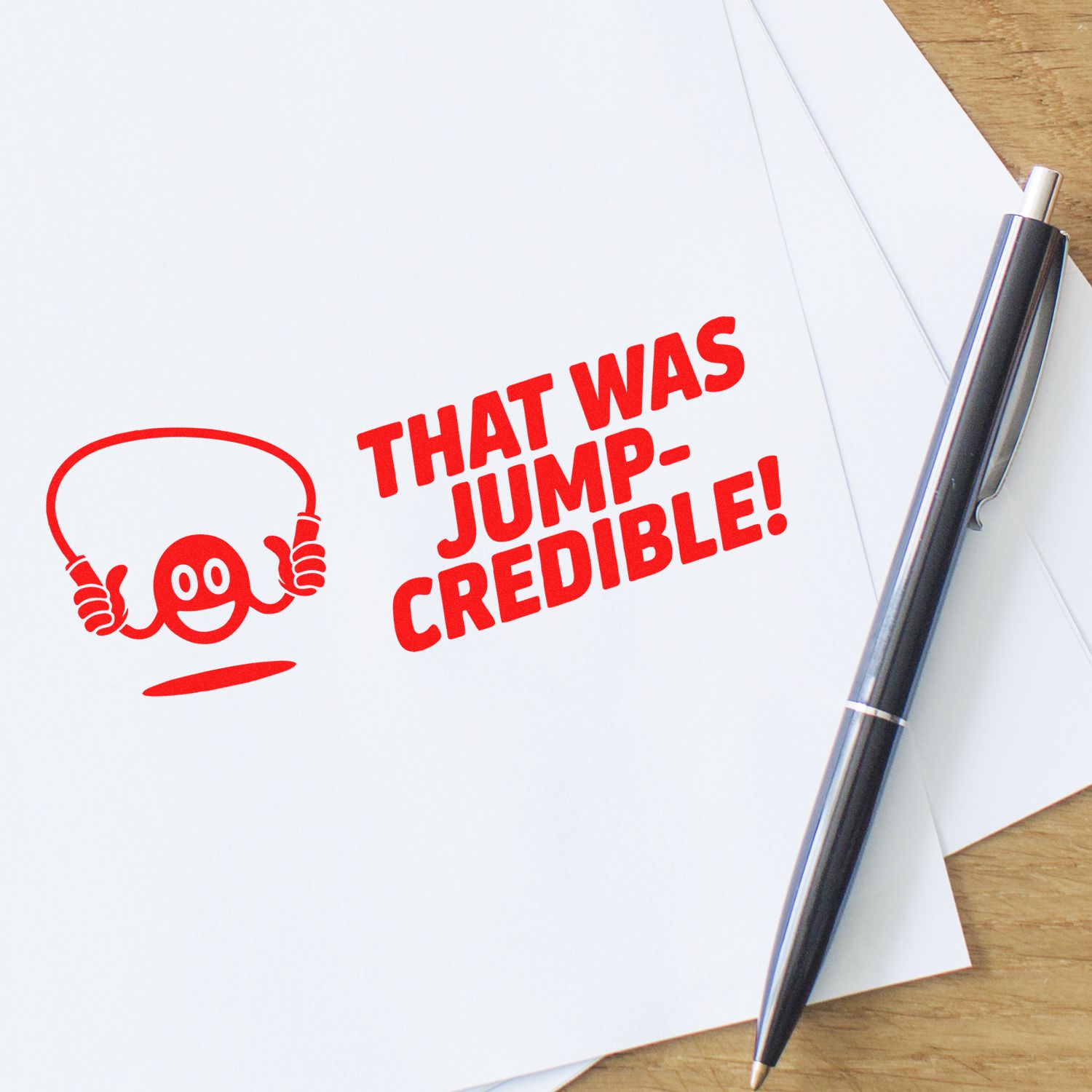 Custom rubber stamp impression reading That Was Jump-Credible! with playful jump rope icon on paper beside a pen.