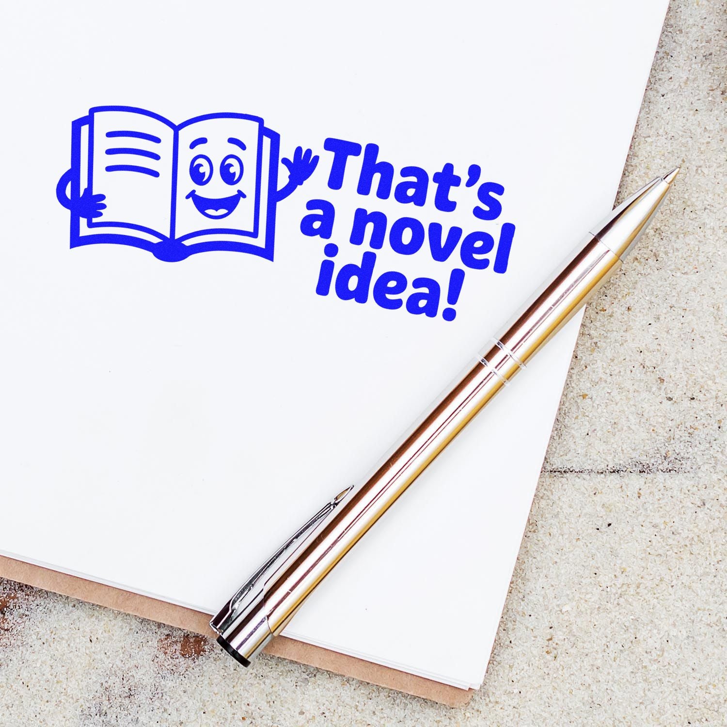 Novel idea rubber stamp design with smiling book icon and Thats a novel idea! text on notebook with pen