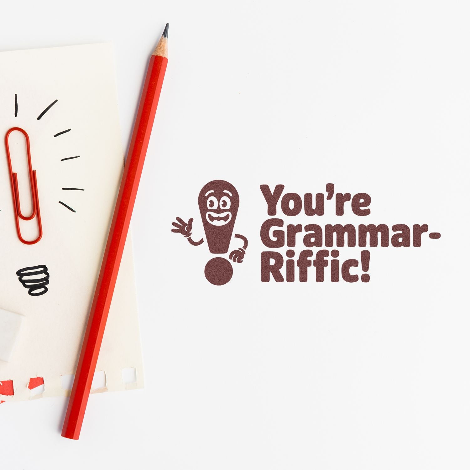 Funny teacher rubber stamp reading Youre Grammar-Riffic! with pencil and paper on a white background.