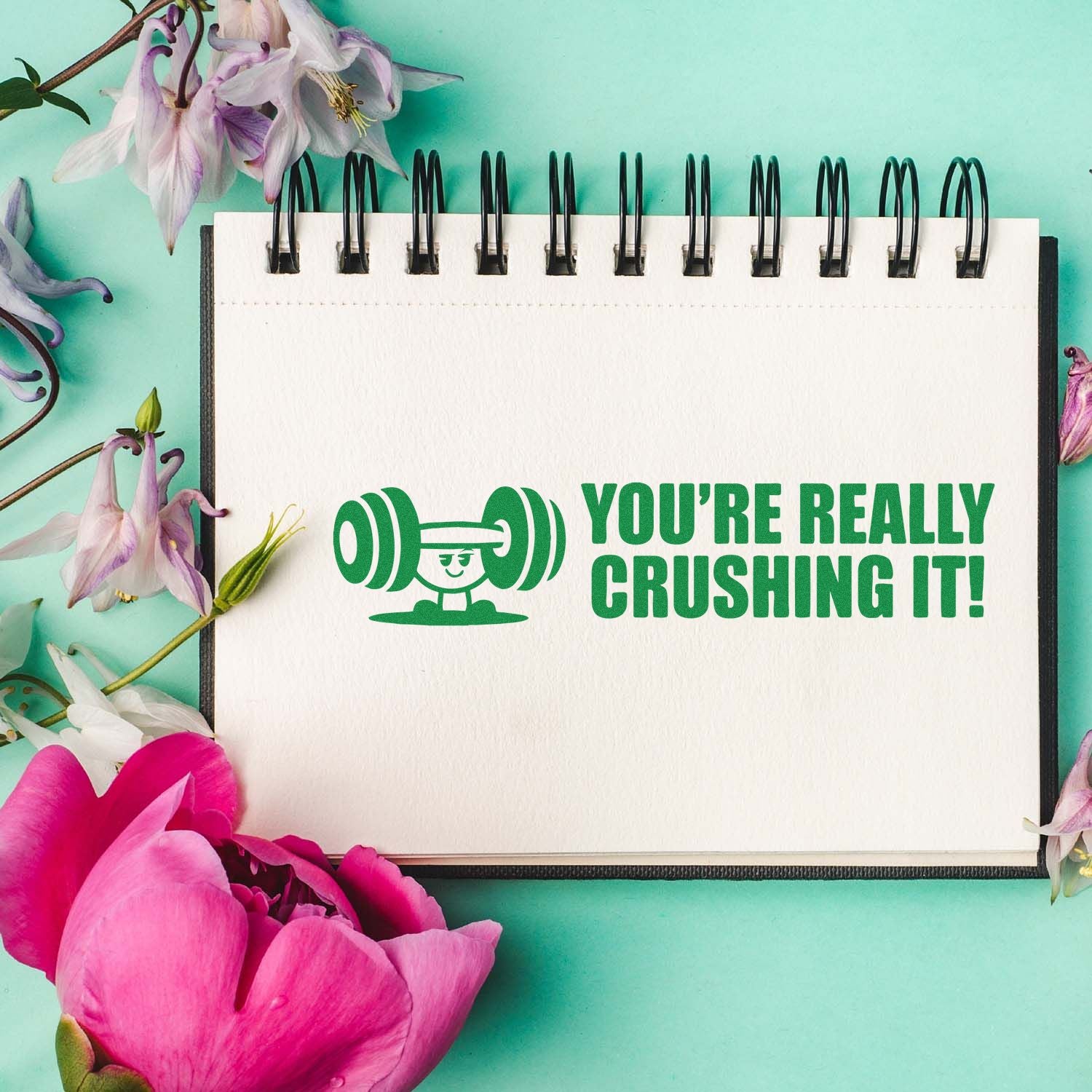 Motivational rubber stamp design reading Youre really crushing it! with weightlifting icon on a notebook.