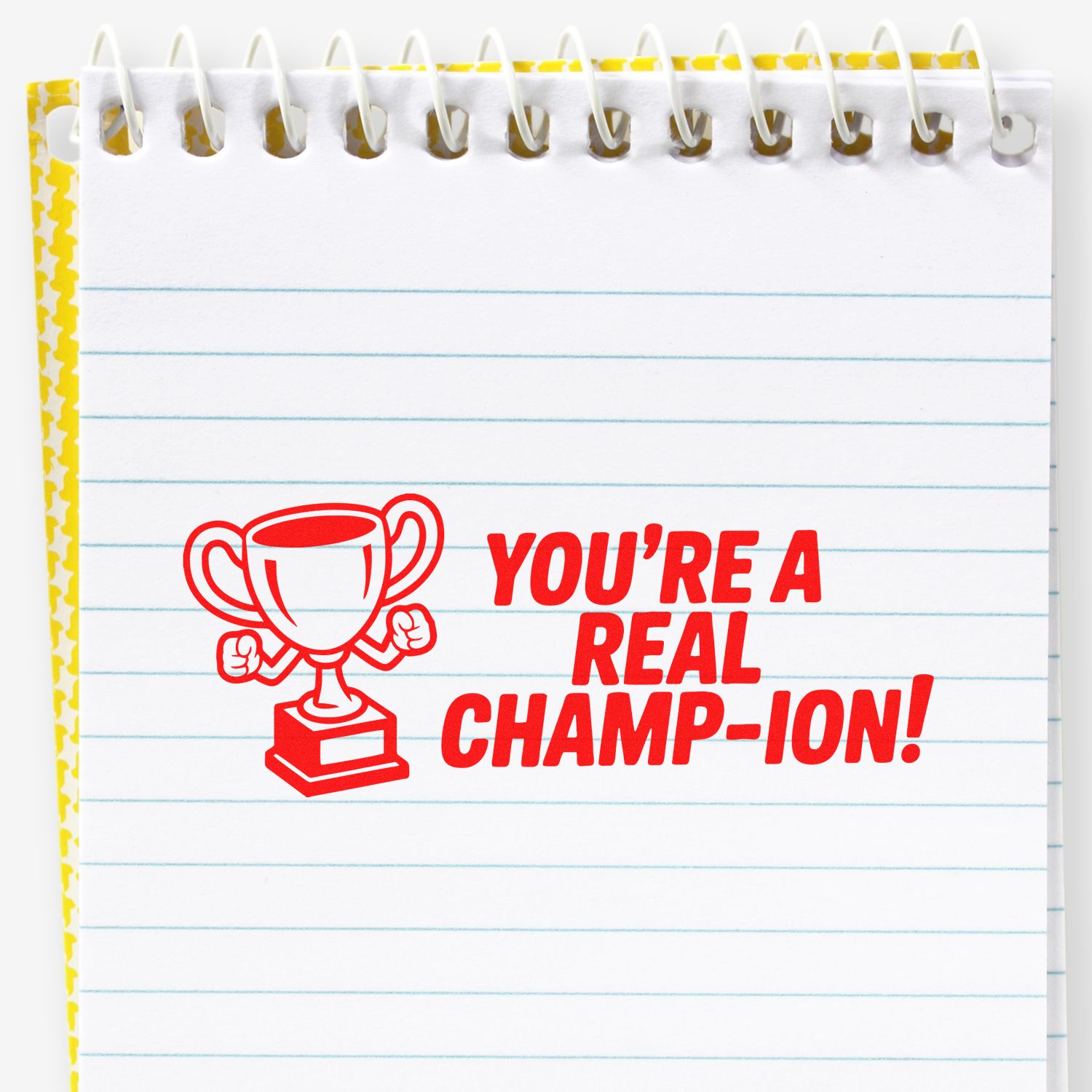 Motivational rubber stamp impression saying Youre a Real Champ-ion! with trophy icon in red ink on notebook paper.