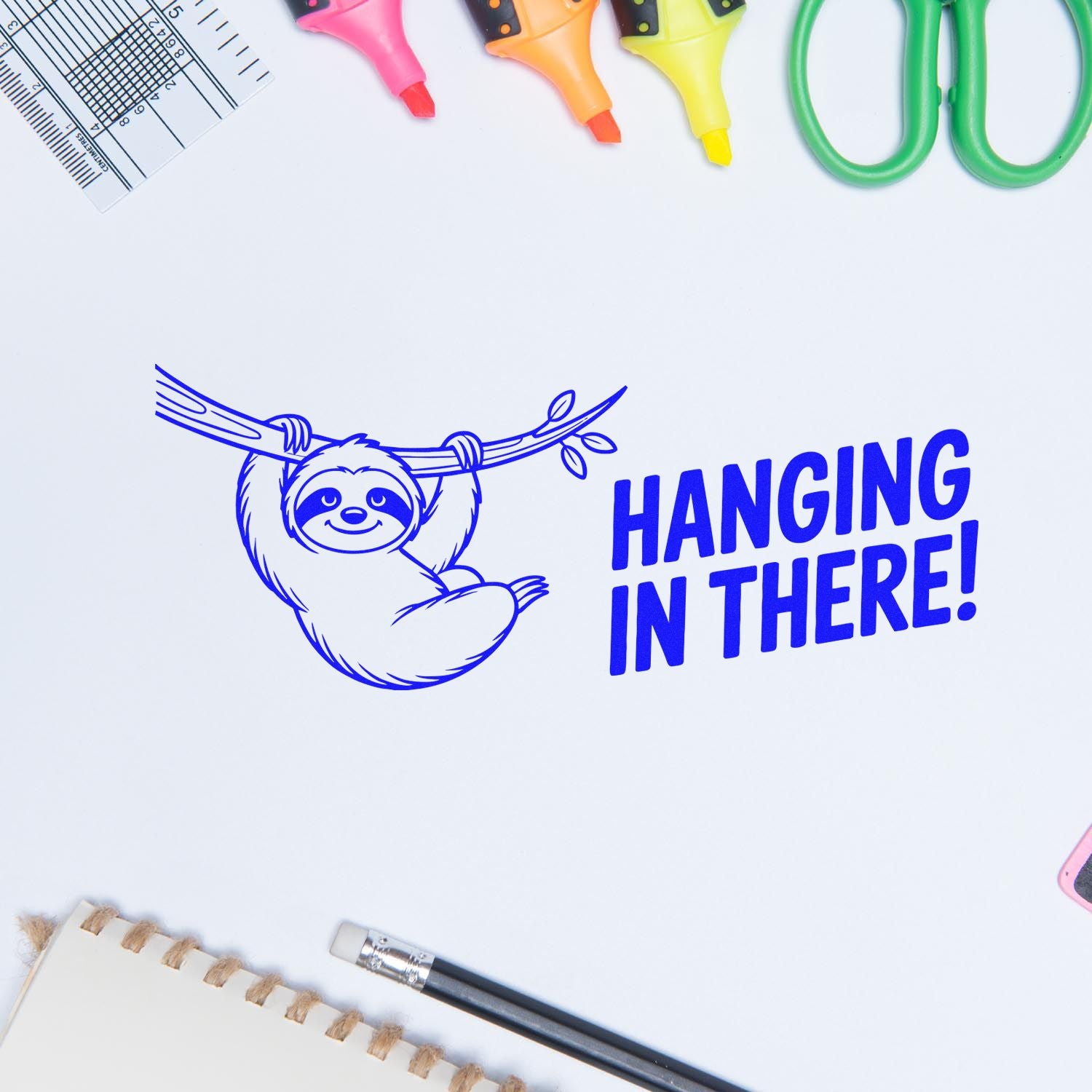 Cute sloth Hanging in There rubber stamp design surrounded by craft supplies on a white background