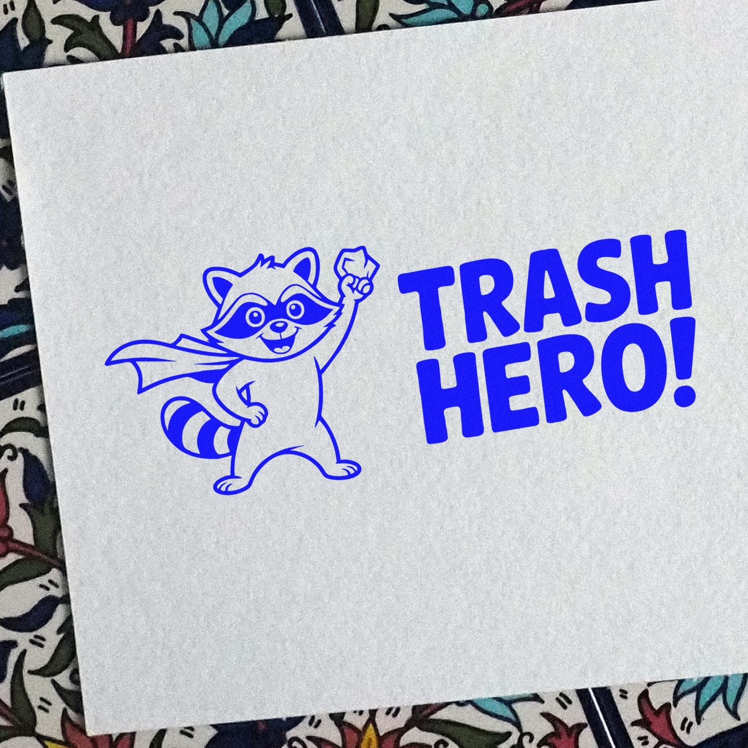 Blue rubber stamp impression of a raccoon superhero with TRASH HERO! text, ideal for custom craft stamps.