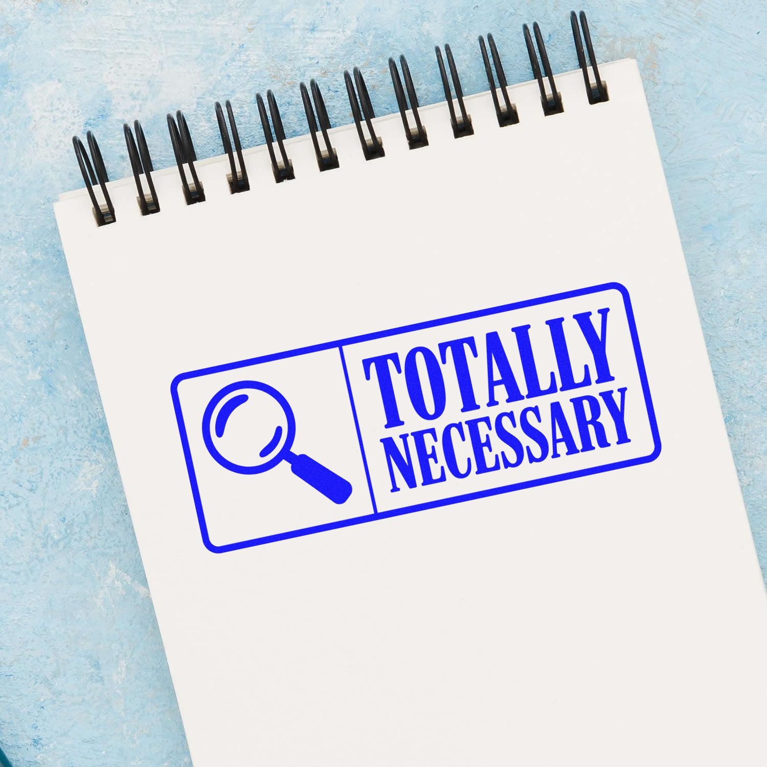 Funny Totally Necessary rubber stamp design with magnifying glass icon on a spiral notebook mockup.