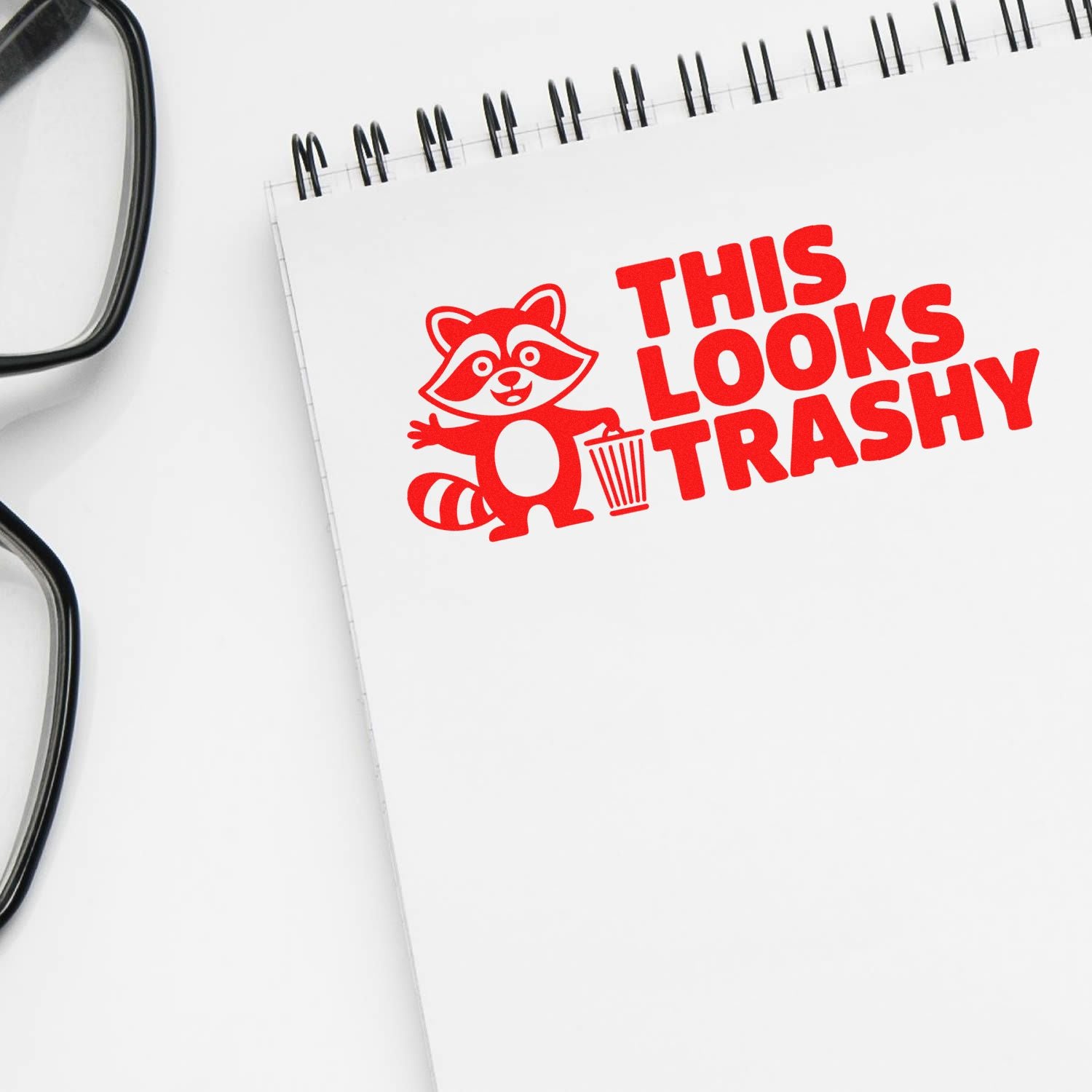 Red rubber stamp design with raccoon and trash can reading This Looks Trashy on a notebook page.