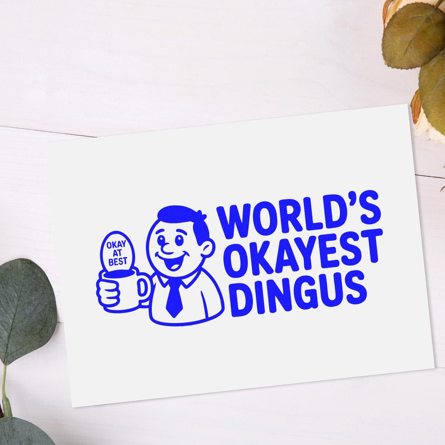 Funny custom rubber stamp design reading Worlds Okayest Dingus with cartoon man holding a mug.