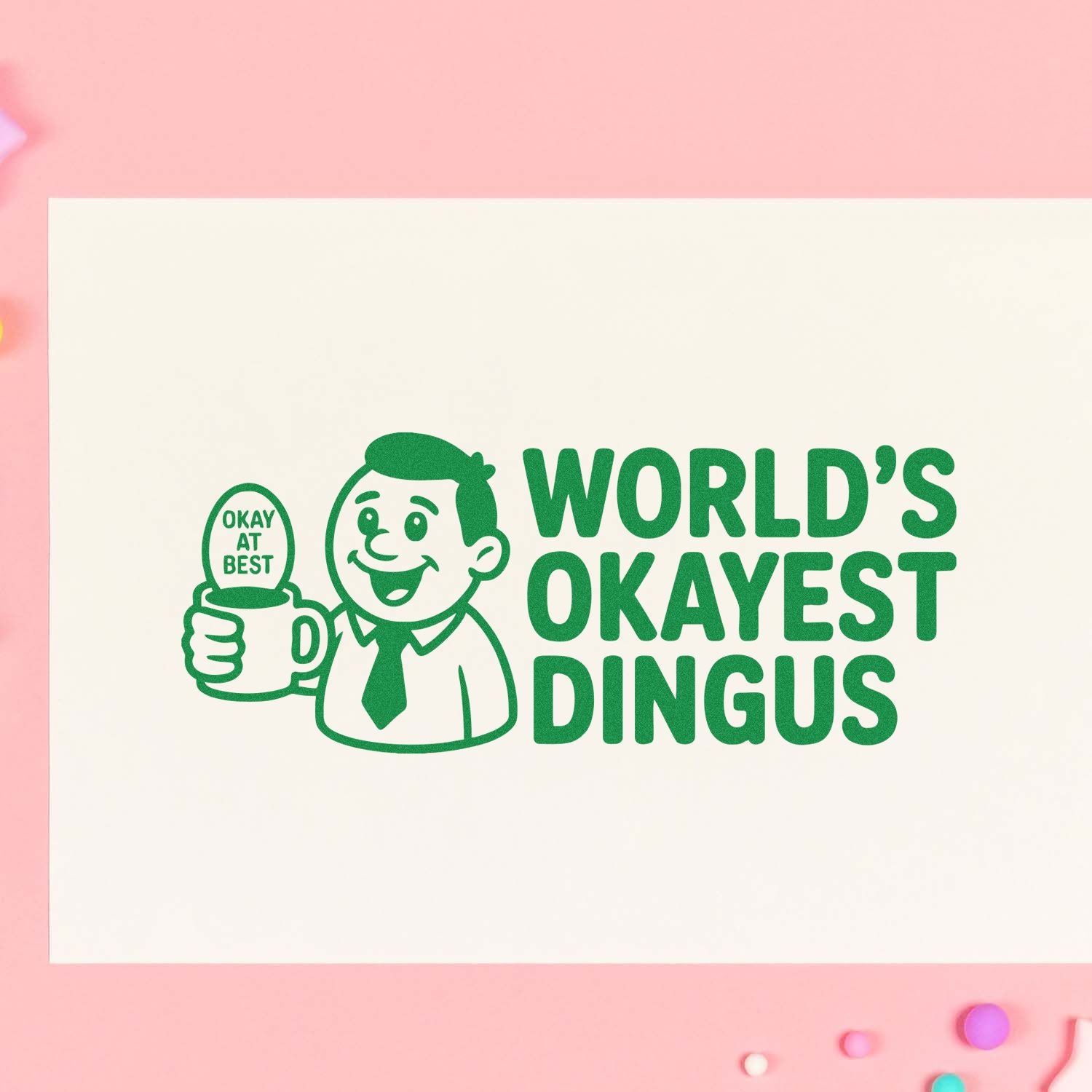 Funny rubber stamp design reading Worlds Okayest Dingus with a cartoon man holding an Okay at Best mug.