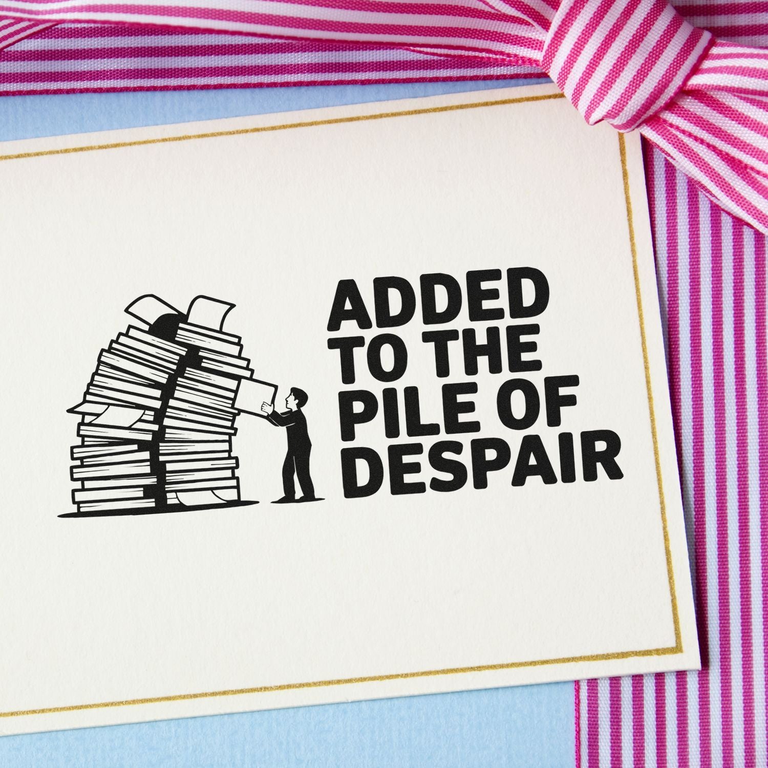 Humorous custom rubber stamp reading Added to the pile of despair with a person pushing paperwork into a stack.