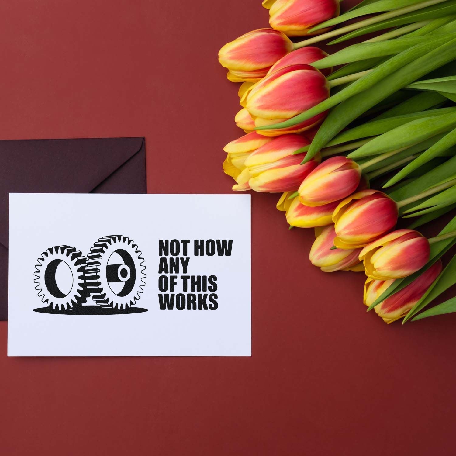 Humorous custom rubber stamp design with gears and Not How Any of This Works on a greeting card beside tulips.