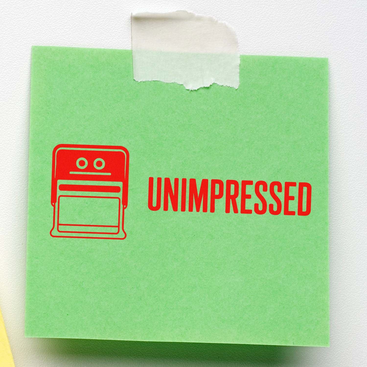 Red Unimpressed rubber stamp design with robot icon stamped on a green sticky note.