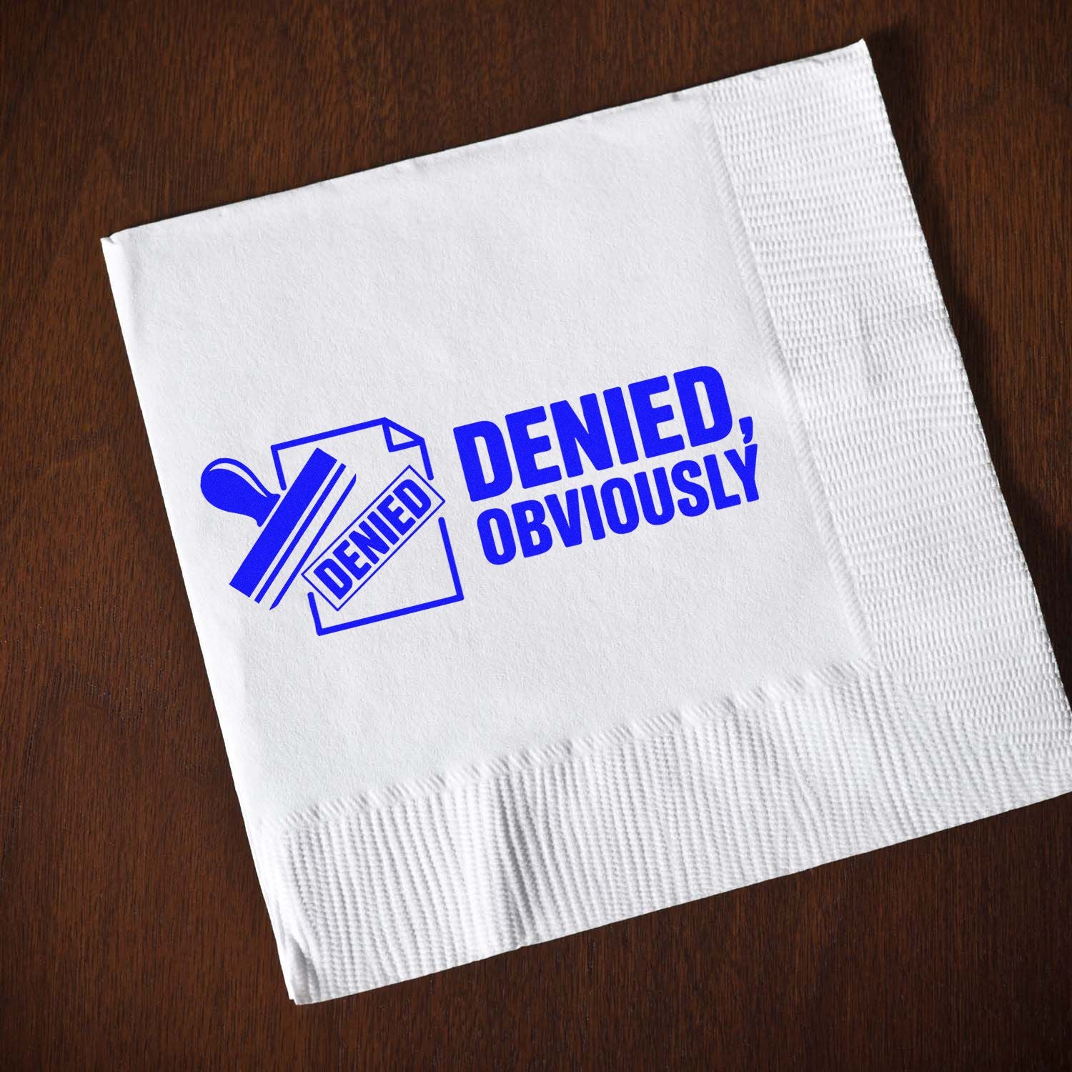 Custom rubber stamp design reading Denied, Obviously stamped in blue on a white napkin.