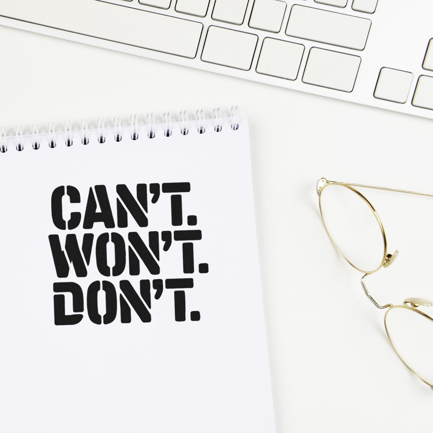 Custom rubber stamp design reading Cant Wont Dont on a notebook, with keyboard and eyeglasses.