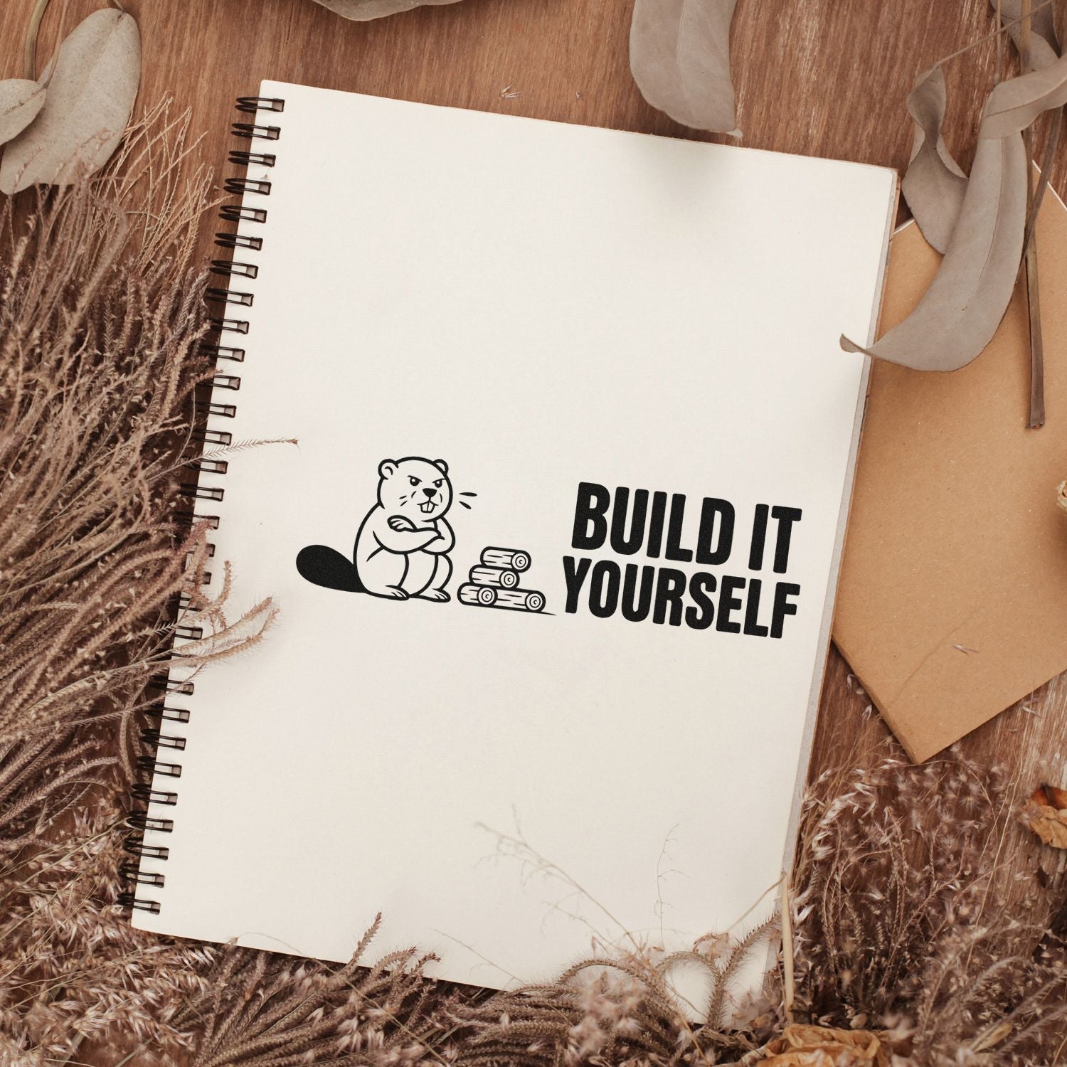 Custom rubber stamp design on notebook reading Build It Yourself with beaver and logs, rustic craft project branding.
