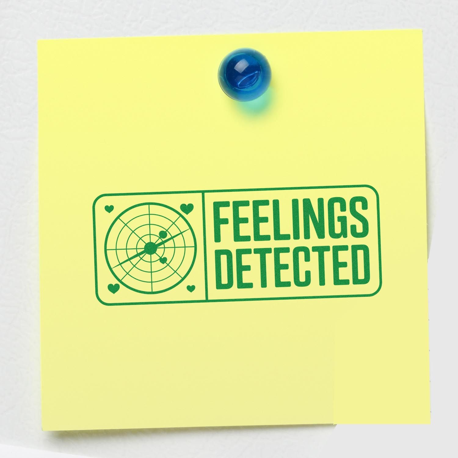 Rubber stamp impression reading FEELINGS DETECTED with radar and hearts on a yellow sticky note, pinned with blue pushpin.
